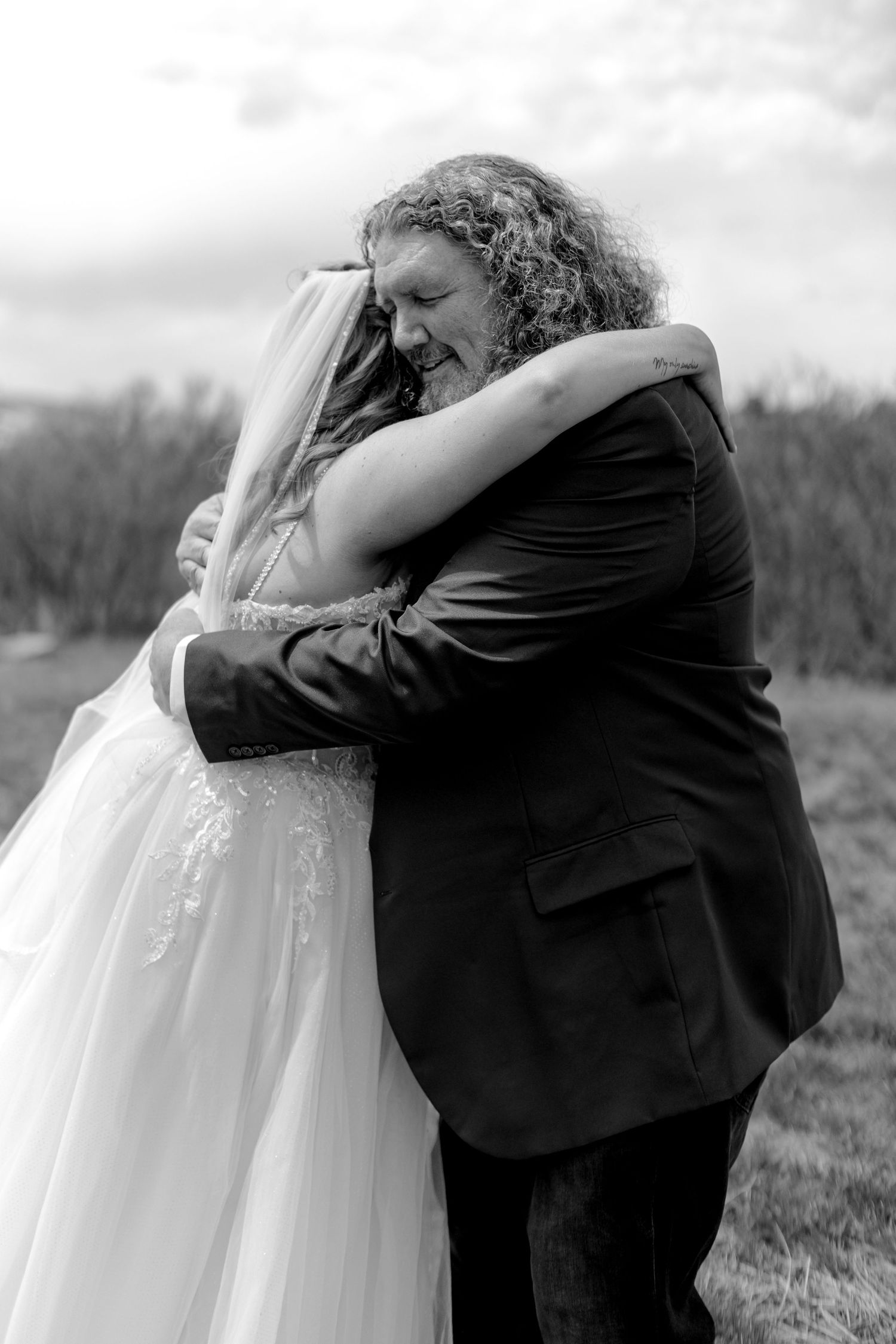 Black and white photo of a bride and groom sharing an emotional embrace outdoors on their wedding day.