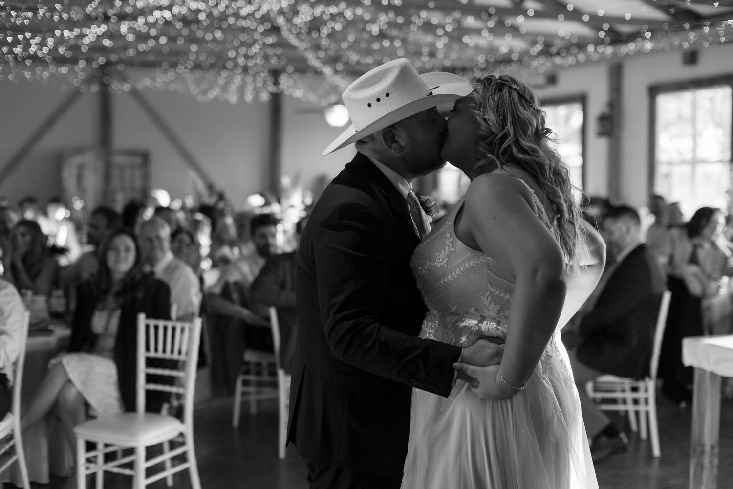 Bride and groom share a first dance kiss in a rustic wedding venue in black and white.