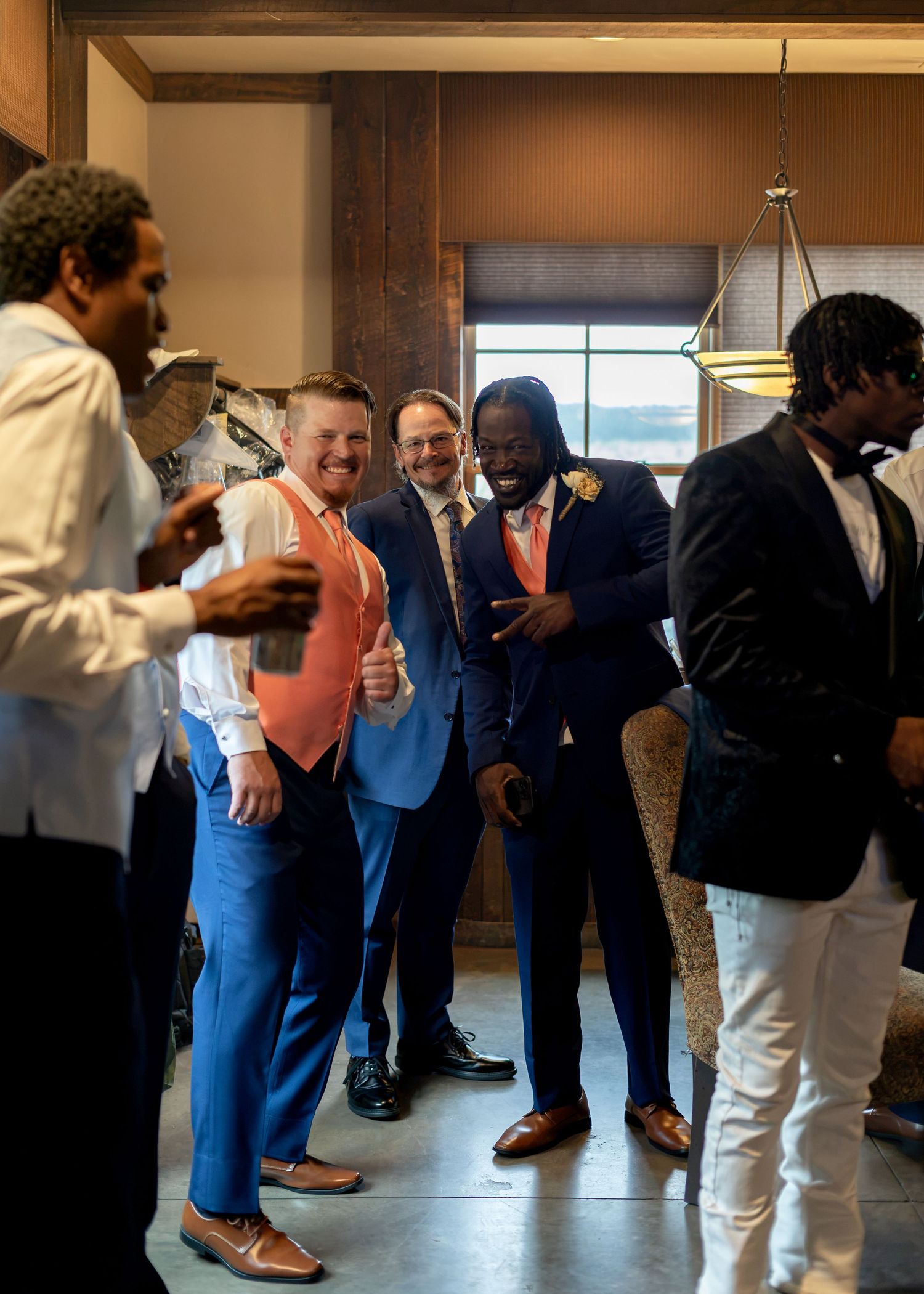 Groomsmen in blue suits and coral vests laughing together indoors before a wedding ceremony.
