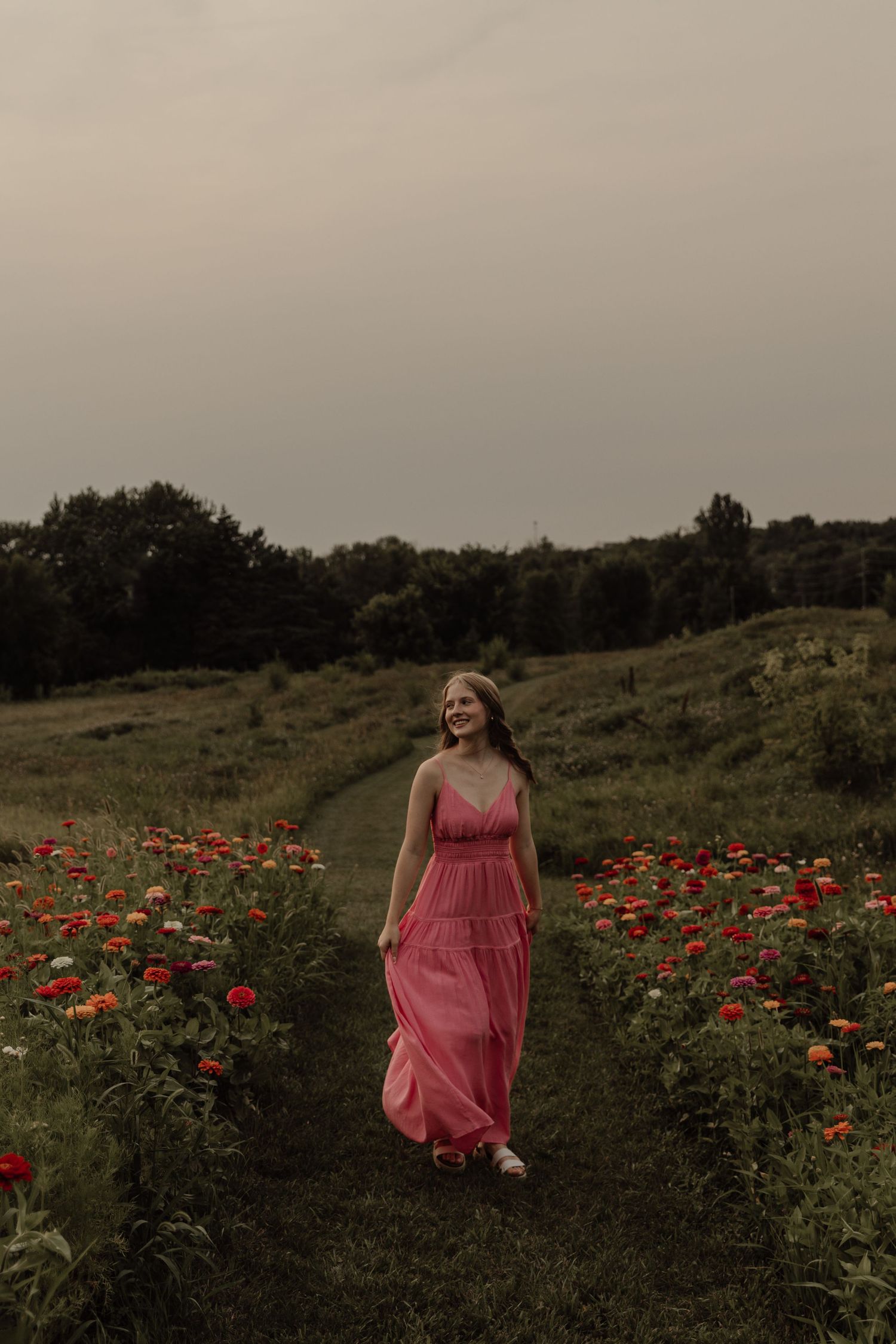 A pink flowy dress stands out against a field of vibrant red poppies at sunset.