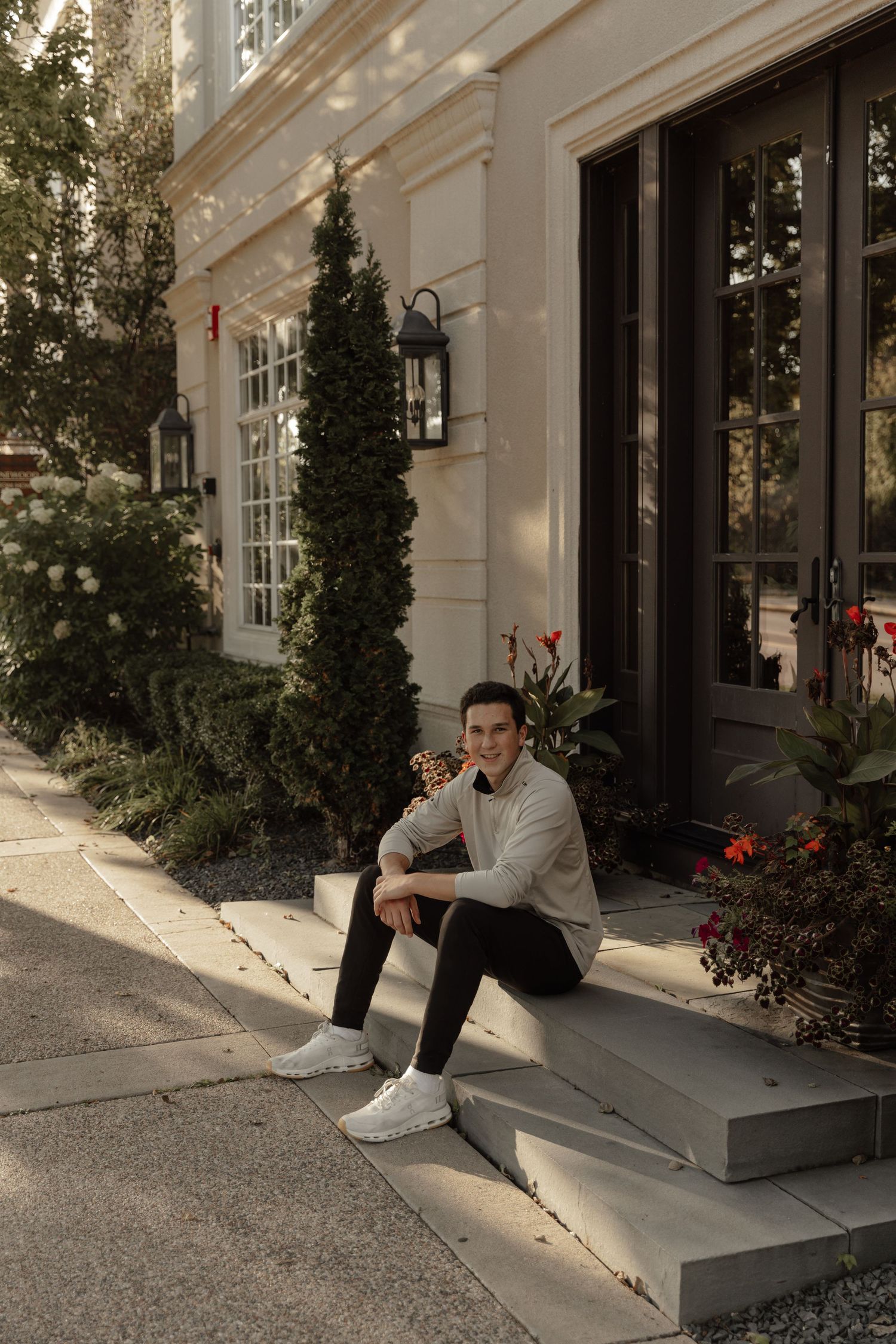Casual portrait of someone sitting on concrete steps outside a building with elegant architecture and greenery.