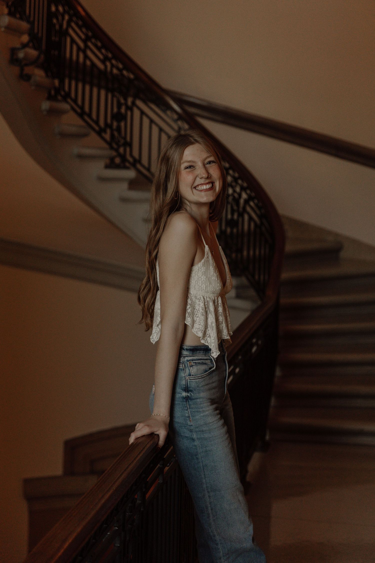 Portrait on an elegant curved staircase with ornate iron railings in warm lighting.