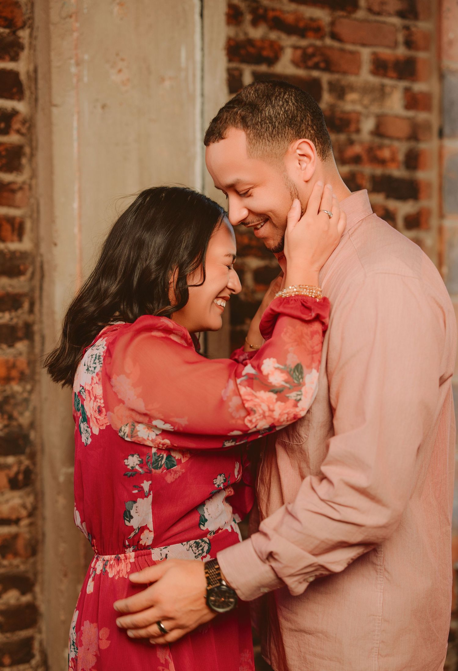 Romantic couple in pink and red clothing share intimate moments in a series of photos against a brick wall.