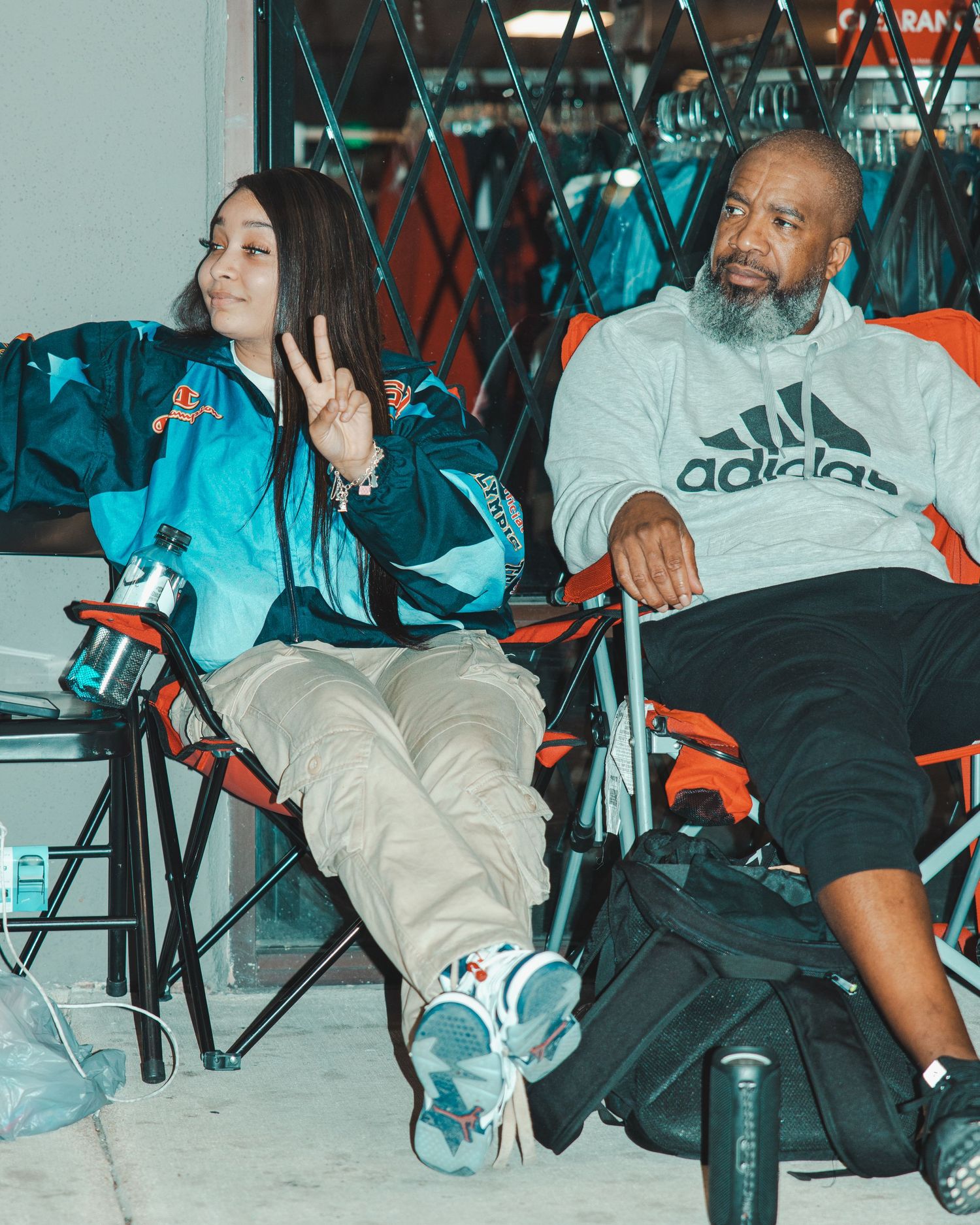 People sitting in chairs wearing casual streetwear and sneakers at an indoor event.