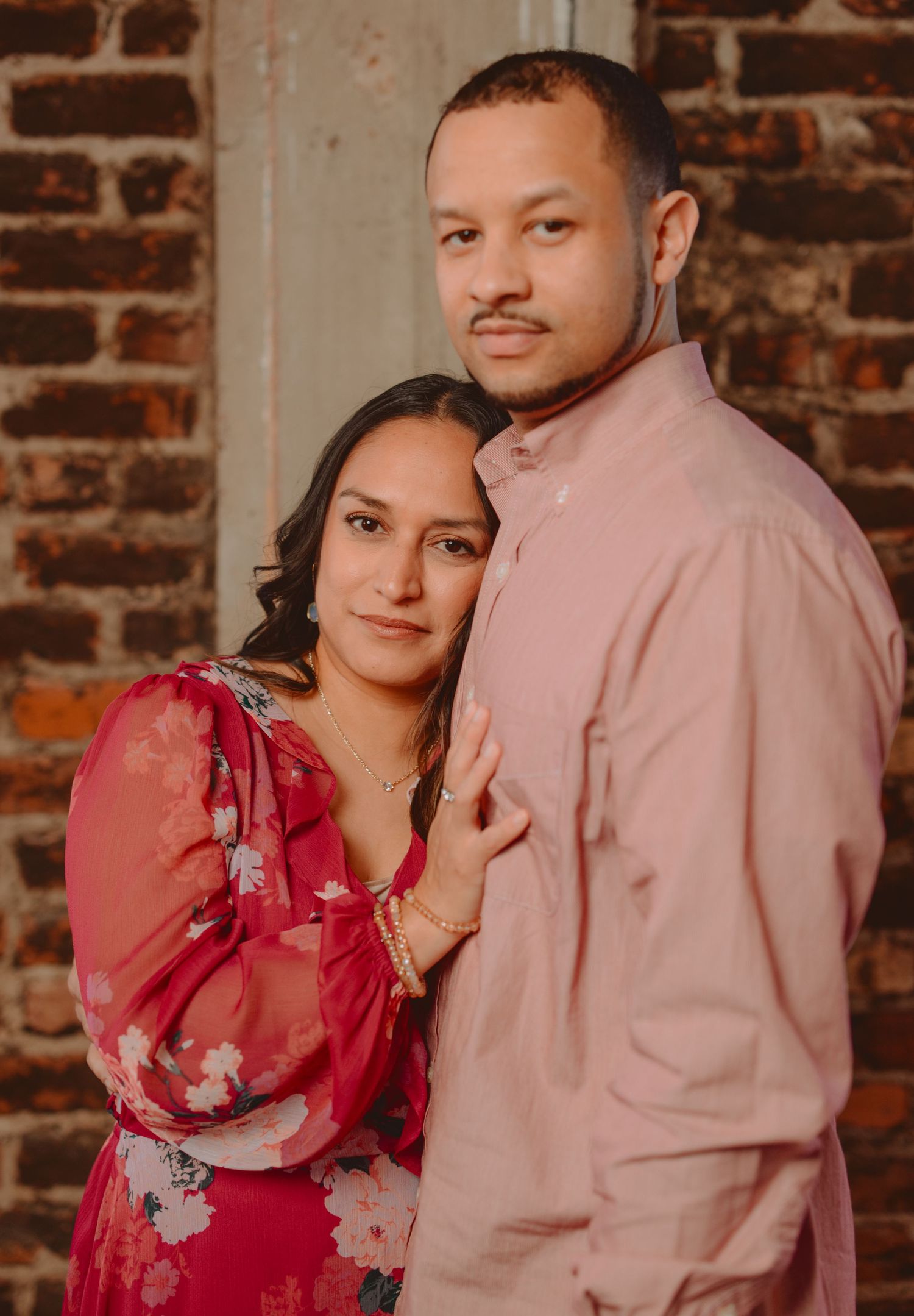 Family portrait against rustic brick wall with pink and red floral outfits.