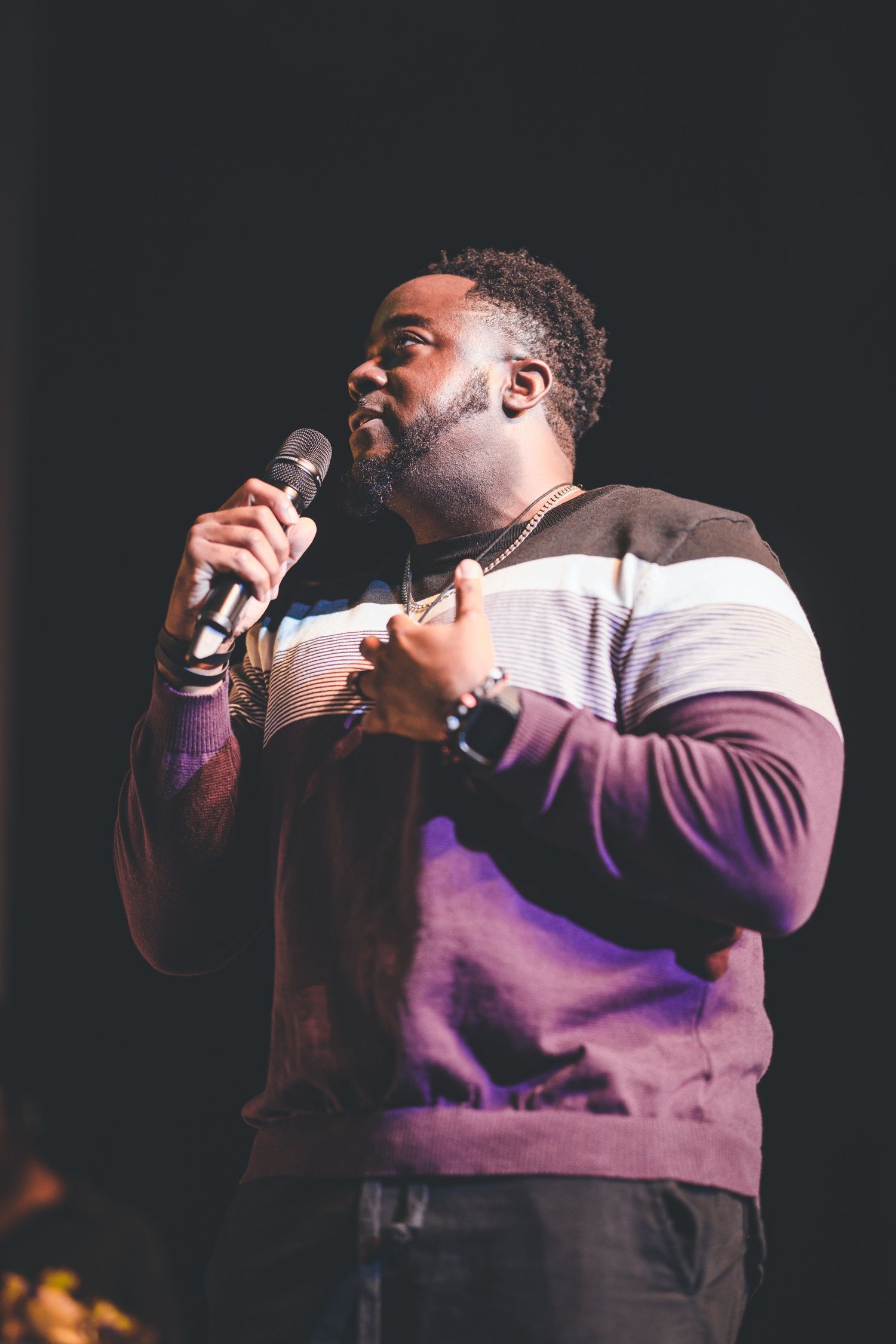 Performer in a purple and white striped sweater passionately singing into a microphone on stage.