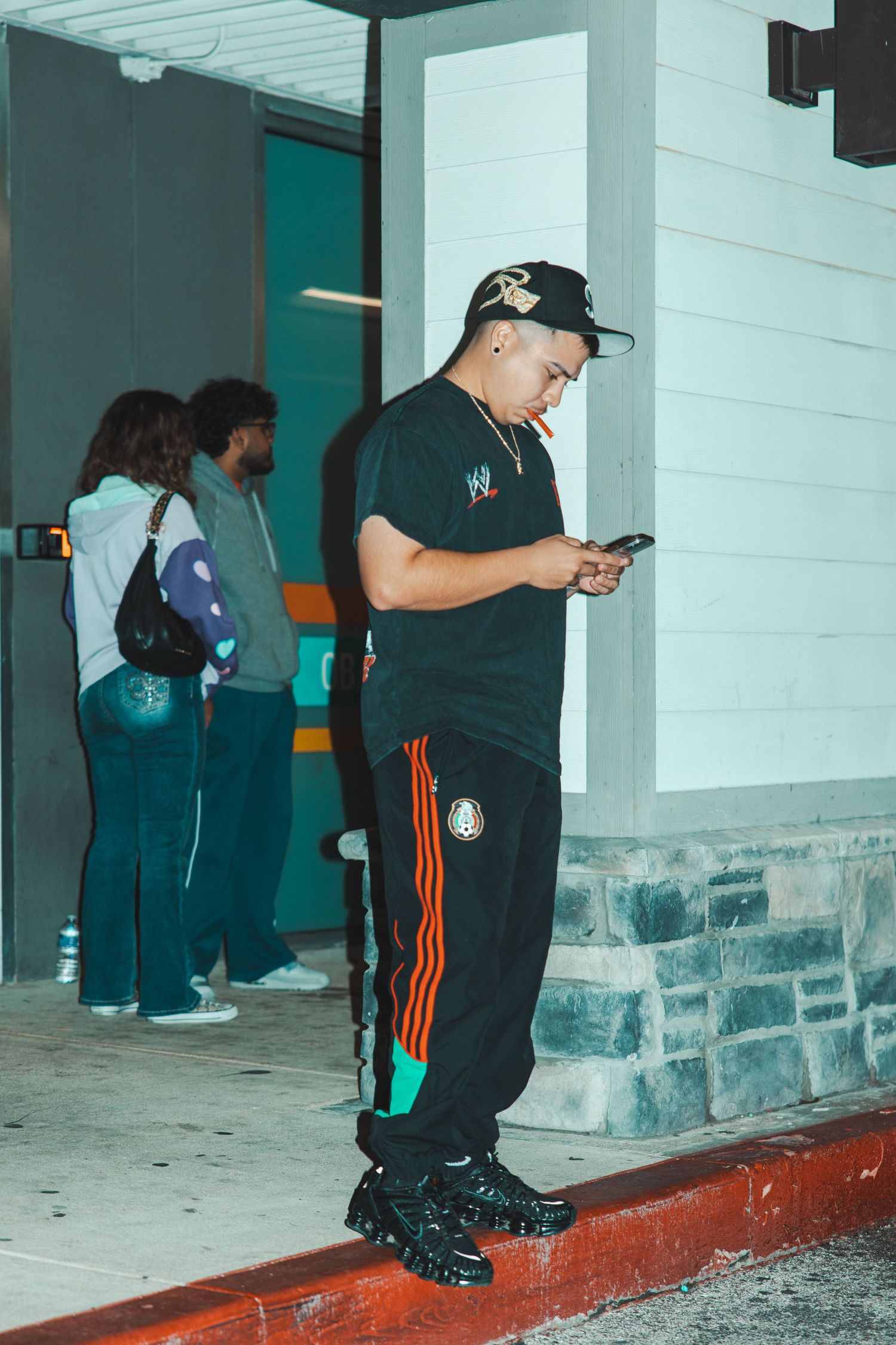 People sitting along a concrete ledge at night checking their phones.