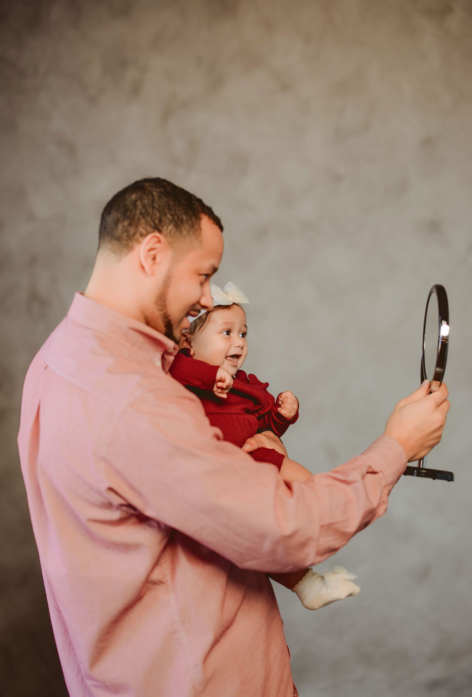 A person in a pink shirt holds a small baby while taking selfie photos in a sequence of candid moments.