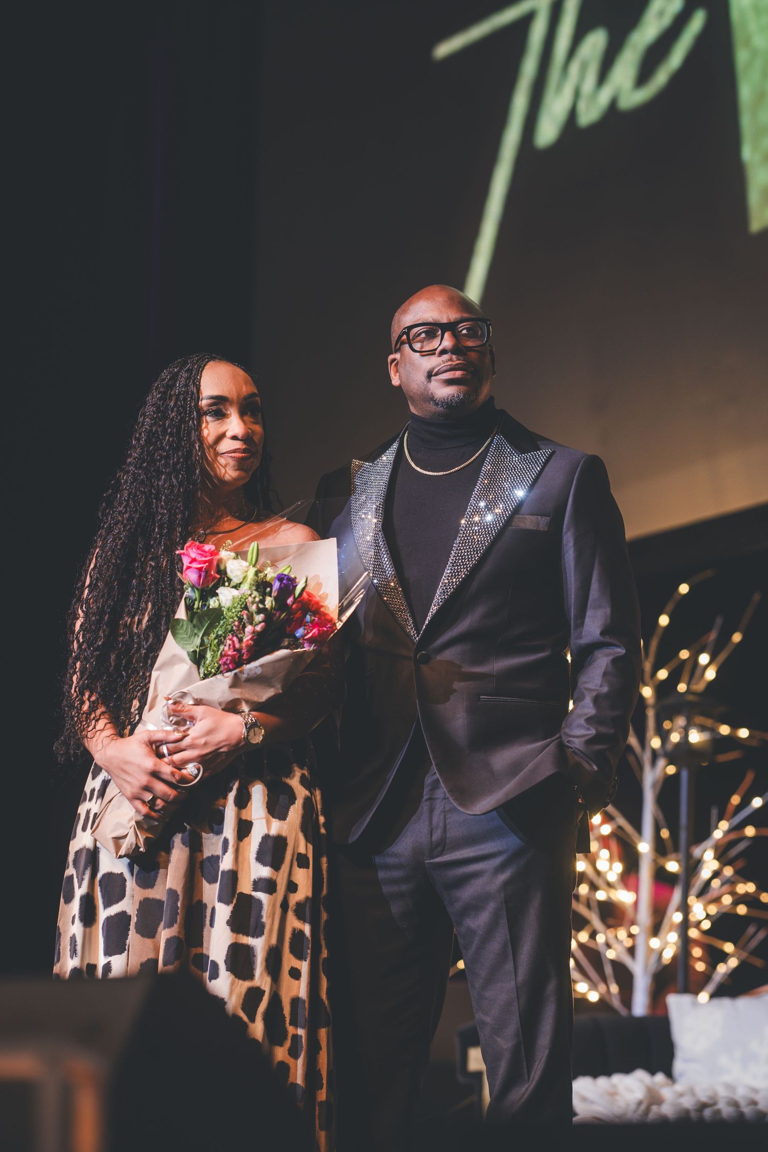Elegant couple on stage with flowers and formal attire during an event.