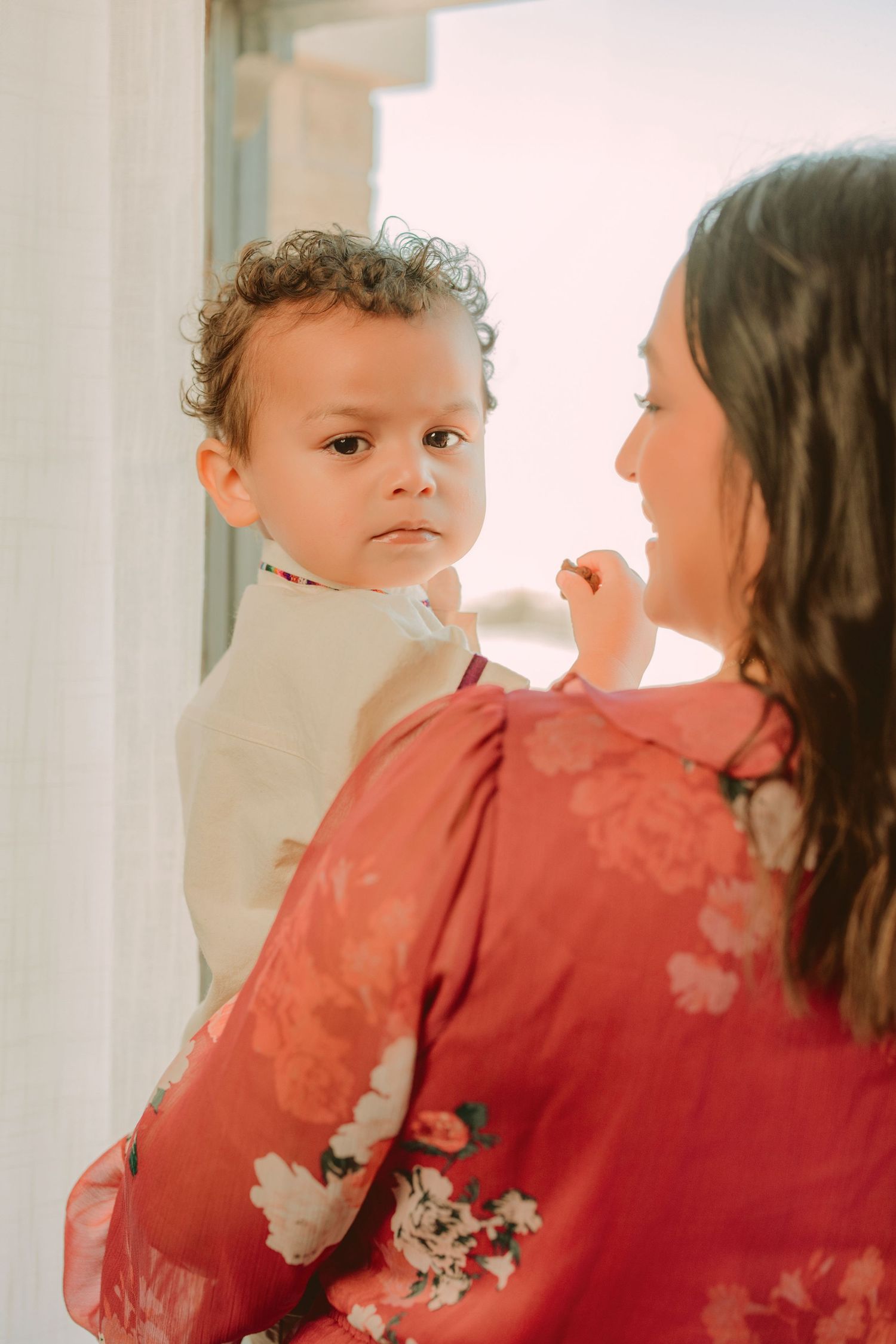 A tender moment captured between a parent and child in red clothing against a bright background.