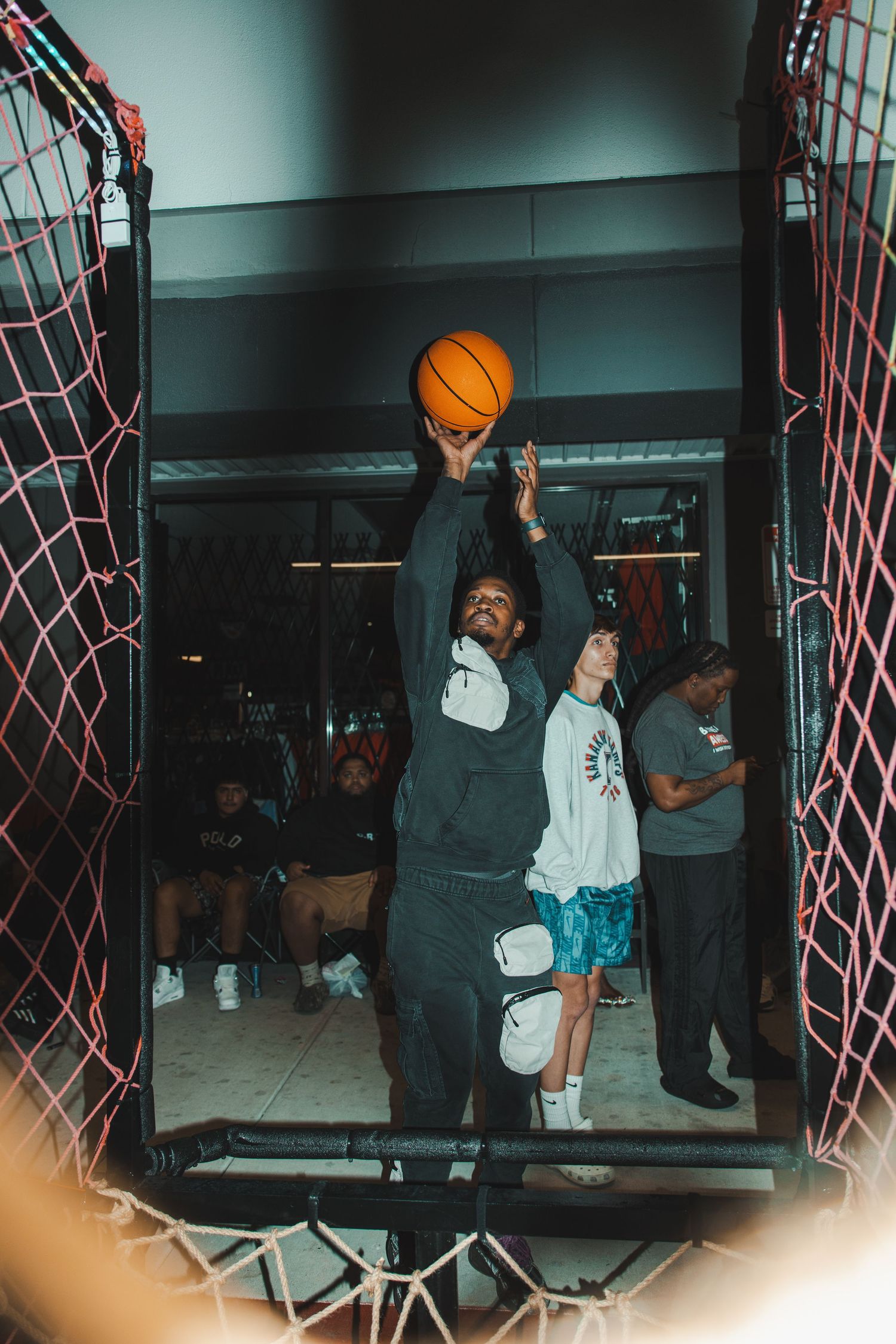 People playing basketball in an indoor court with red nets visible in the frame.