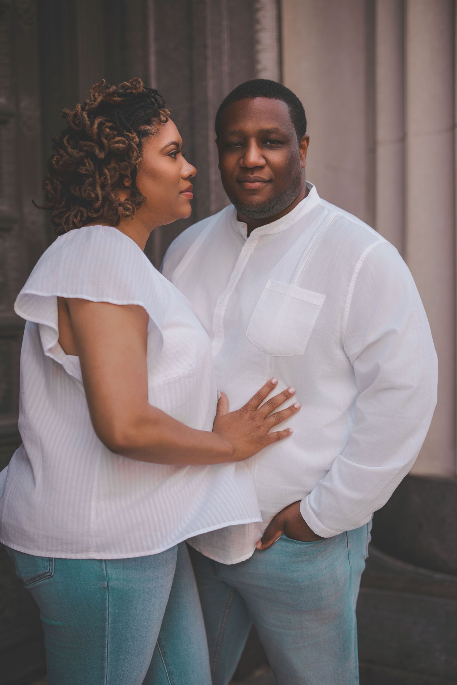 A couple in matching white tops and teal pants embraces during an outdoor photoshoot.