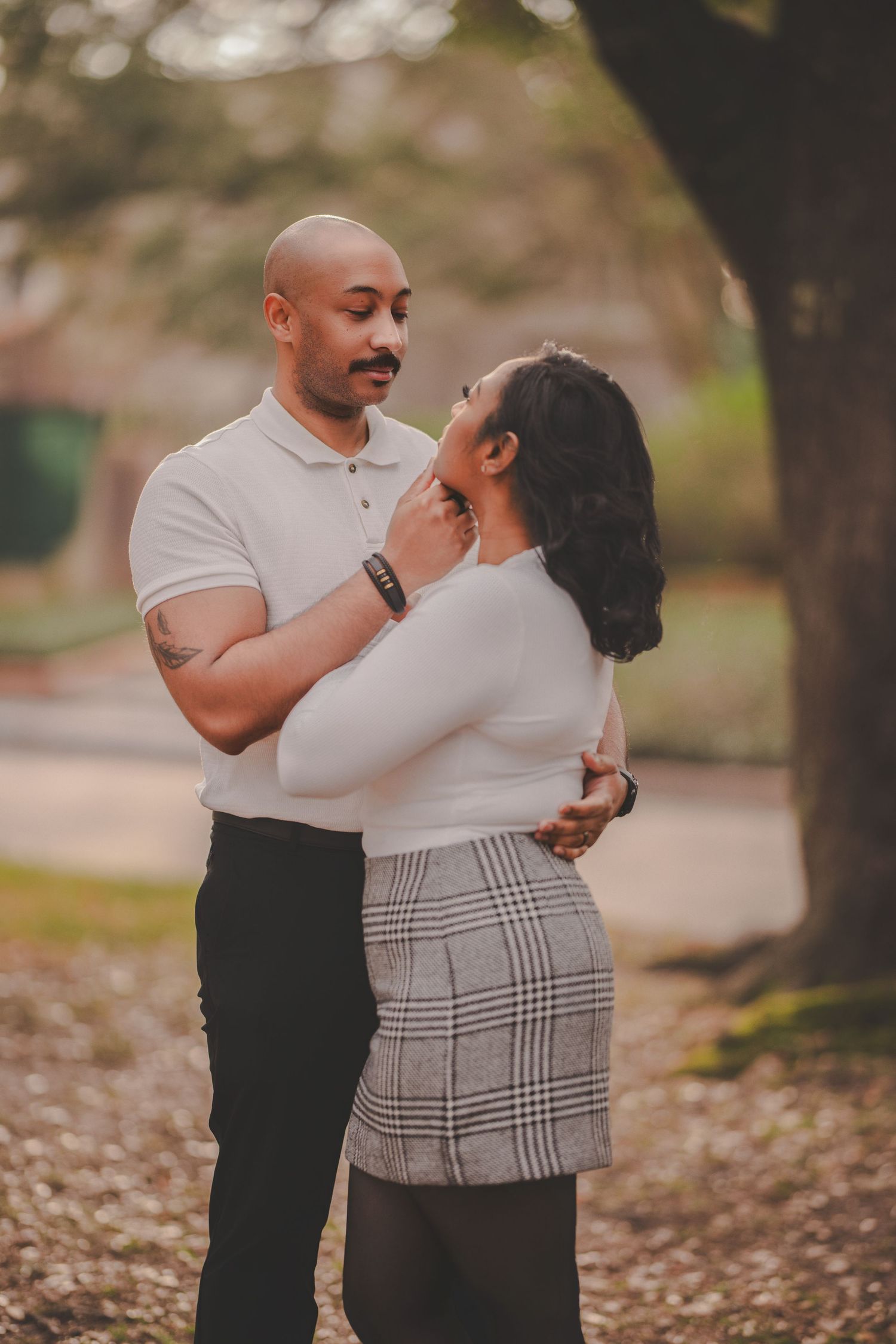 A loving couple embraces while standing on fallen autumn leaves in a park setting.