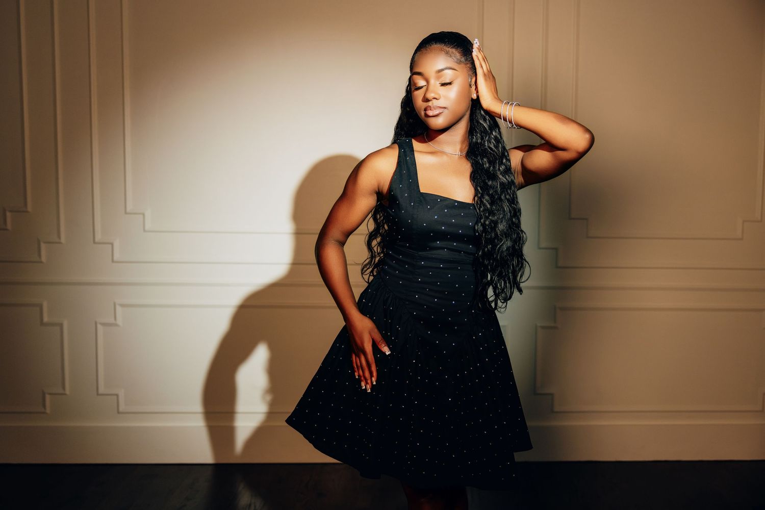A person in a black dress poses confidently against a beige wall in a series of artistic portraits.