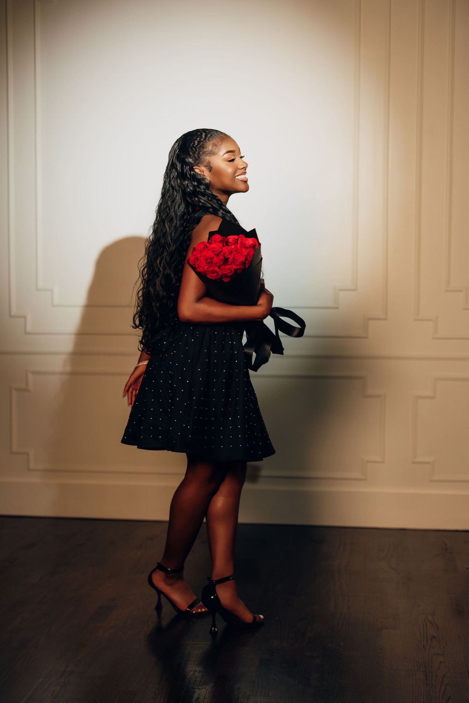 A series of five photos showing a person in a black dress and red bag twirling and dancing against a beige wall.