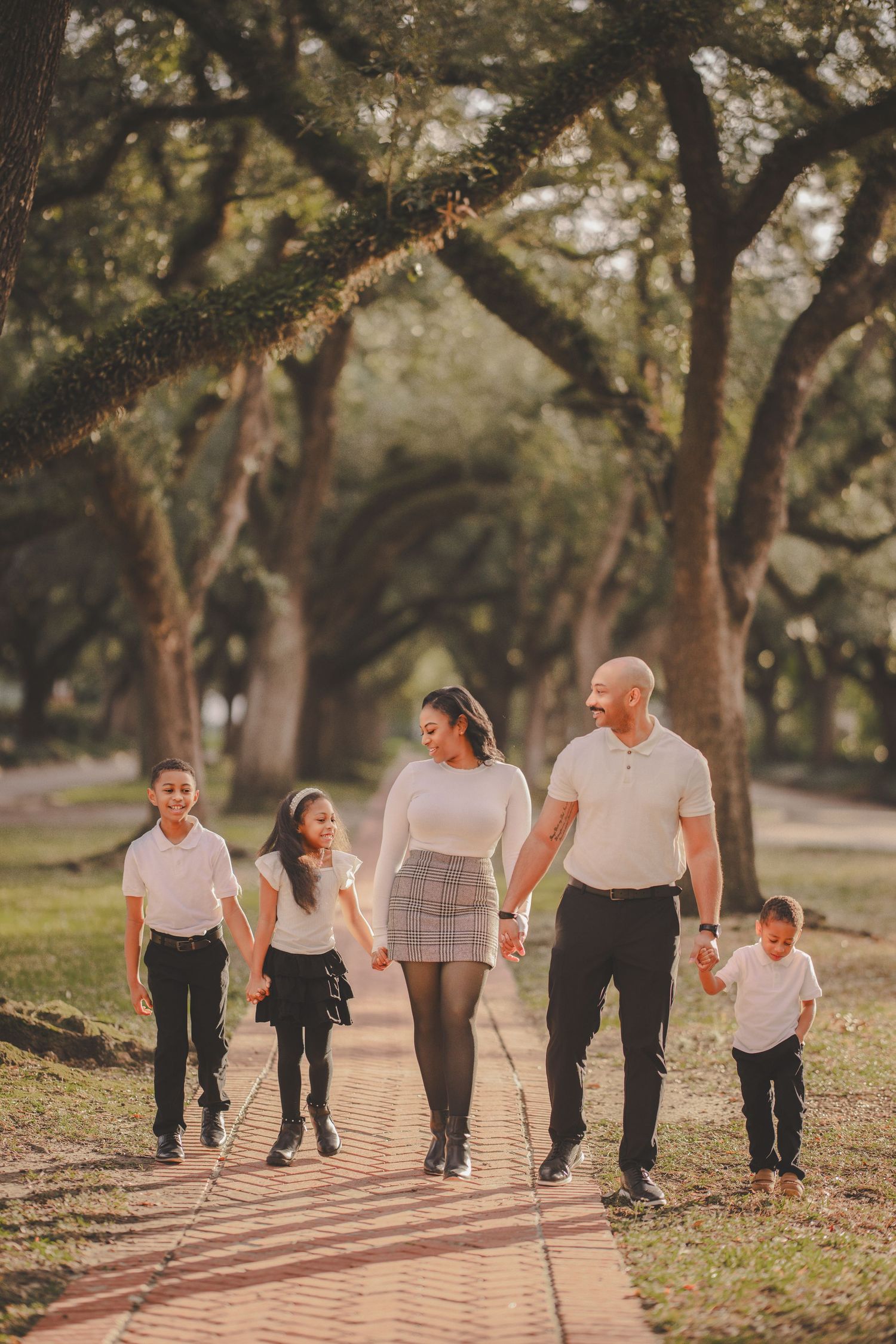 A group walks together on a sunlit path through a wooded park during golden hour.