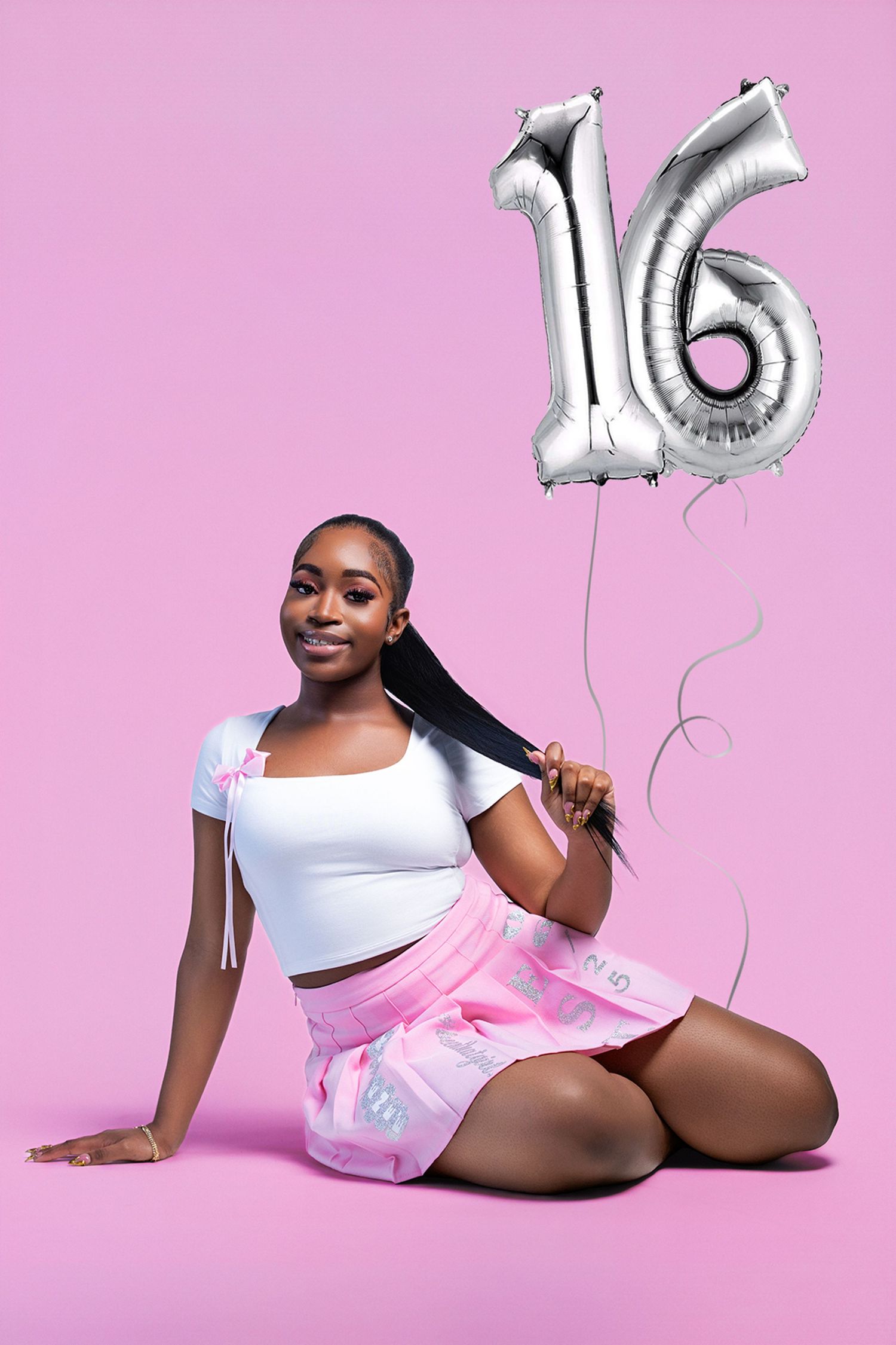 Woman in white outfit poses playfully on pink background with silver number balloons.