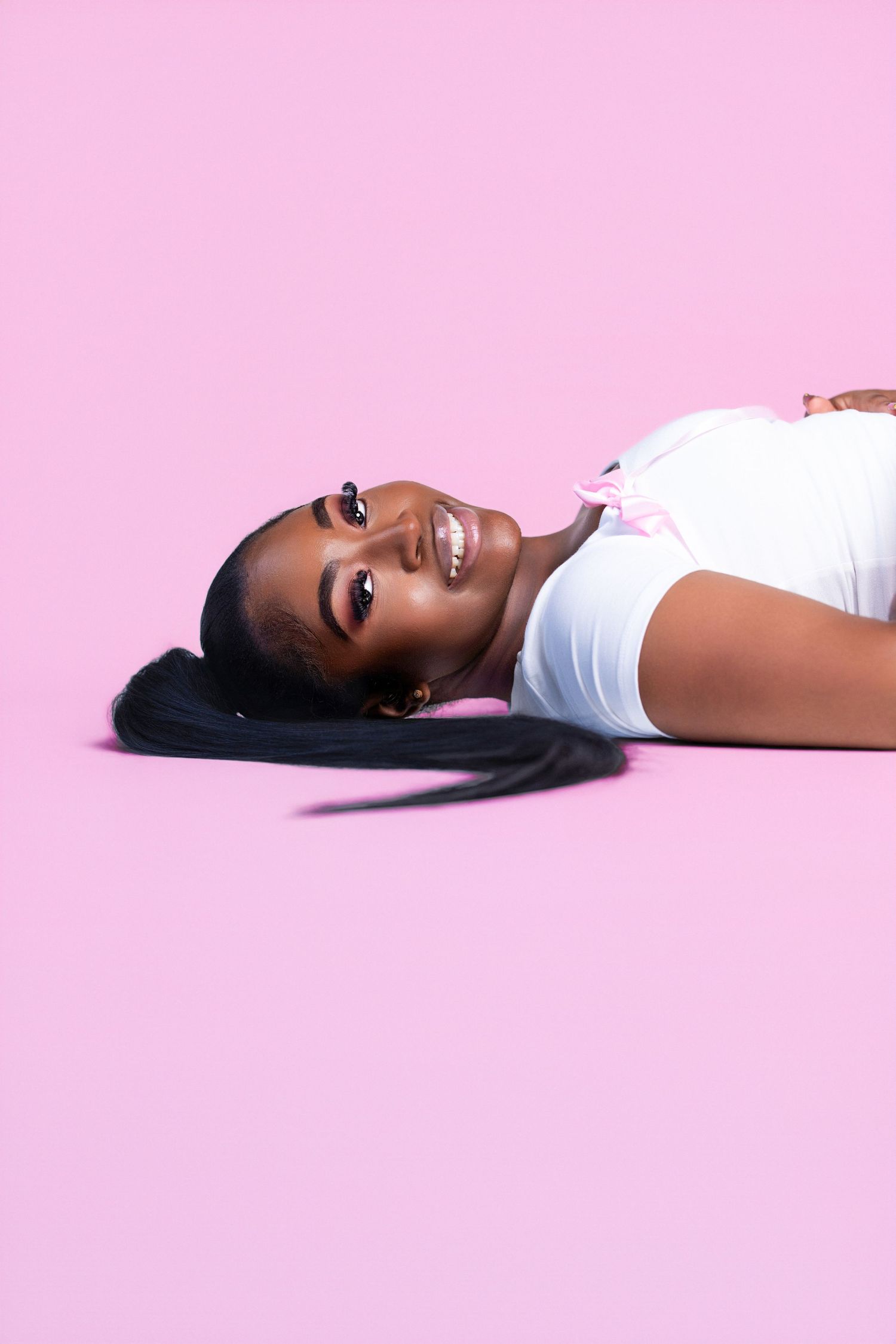 Woman in white top poses gracefully on pink background in artistic photoshoot.