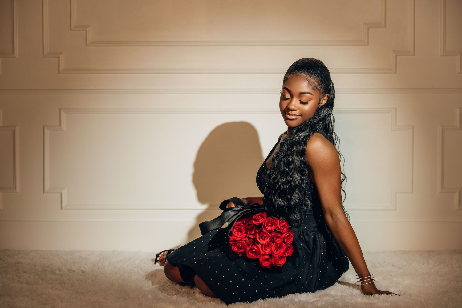 A model in a black tulle dress poses elegantly on the floor with a red floral accent.