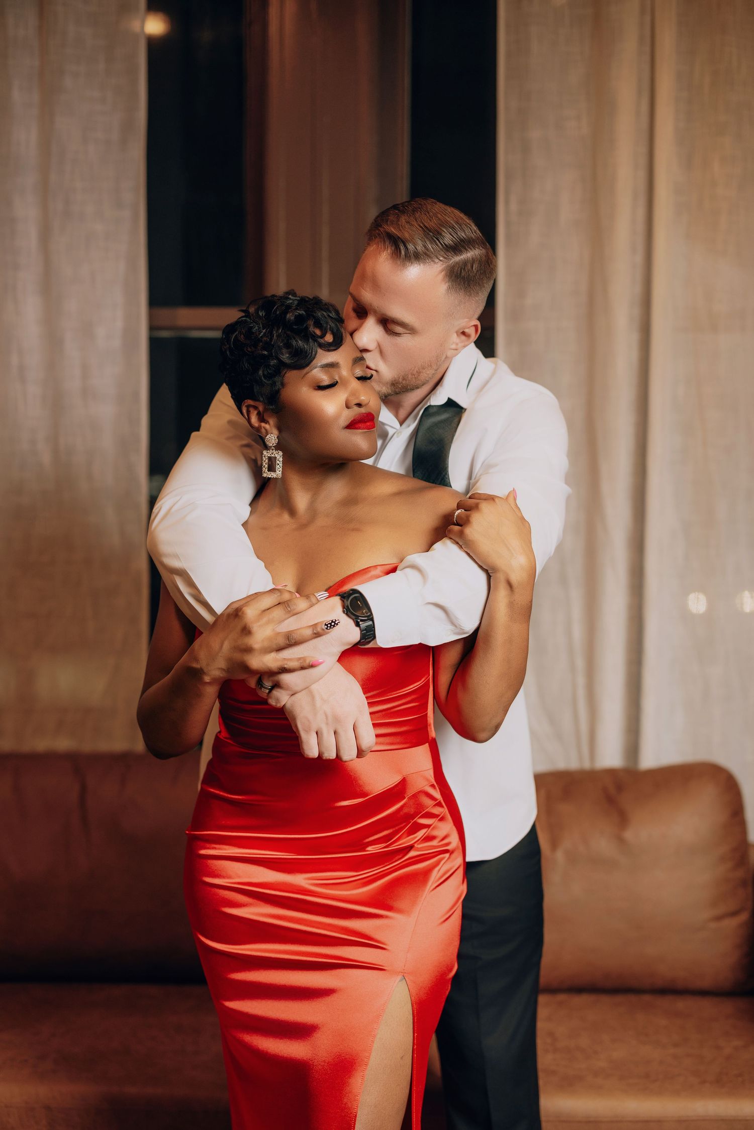 A couple dances intimately in a dimly lit room, with the woman wearing a striking red satin dress.