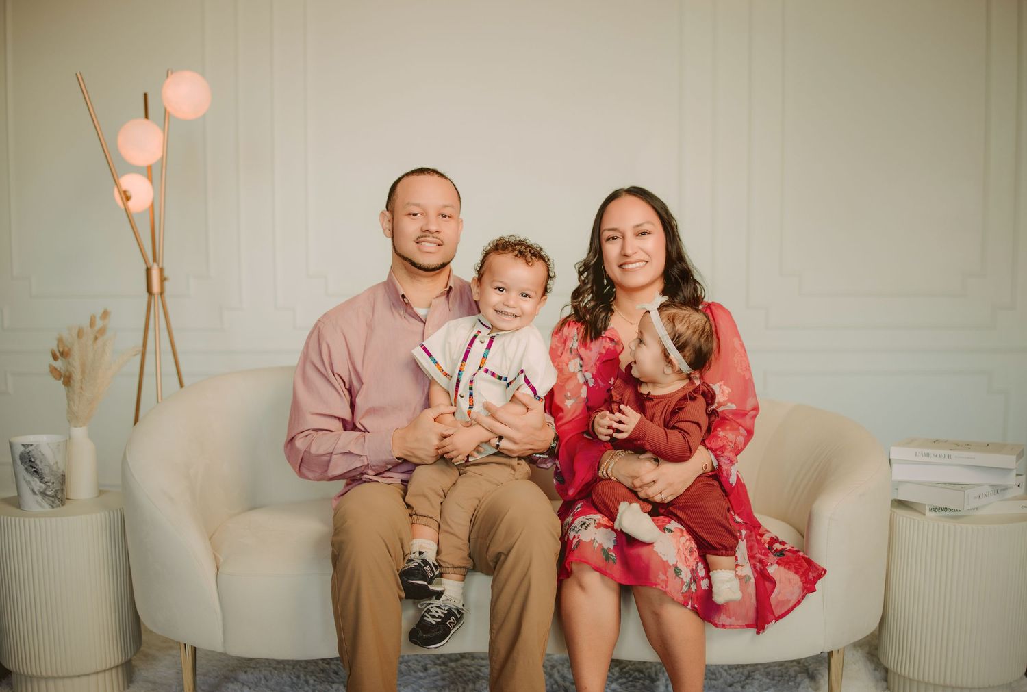 Family in coordinating outfits poses together on couch with pink balloons for indoor photo session.