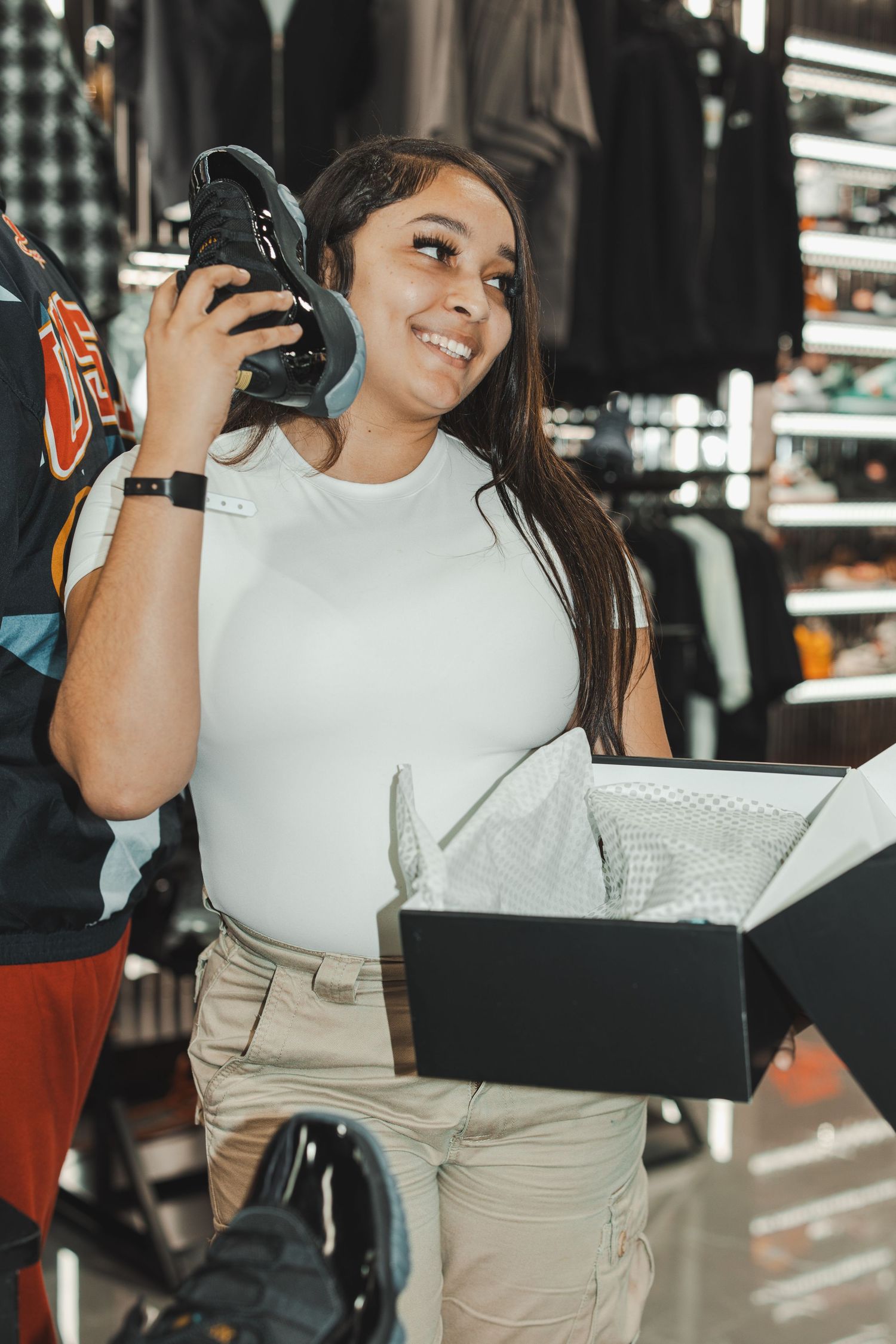 Customer in white top holding shoe boxes and smiling at sneaker store.