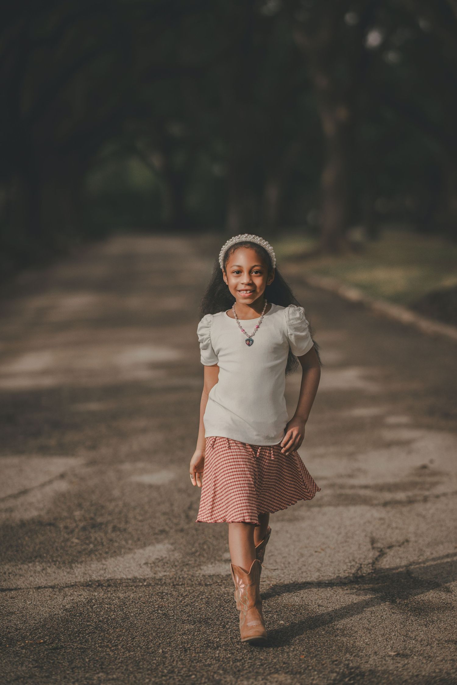 Young person in a gray top and pink skirt walks confidently on a tree-lined path.