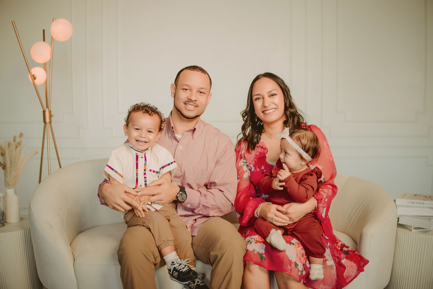 Family portrait on beige couch with pink balloons, featuring parents with two young children in formal attire.