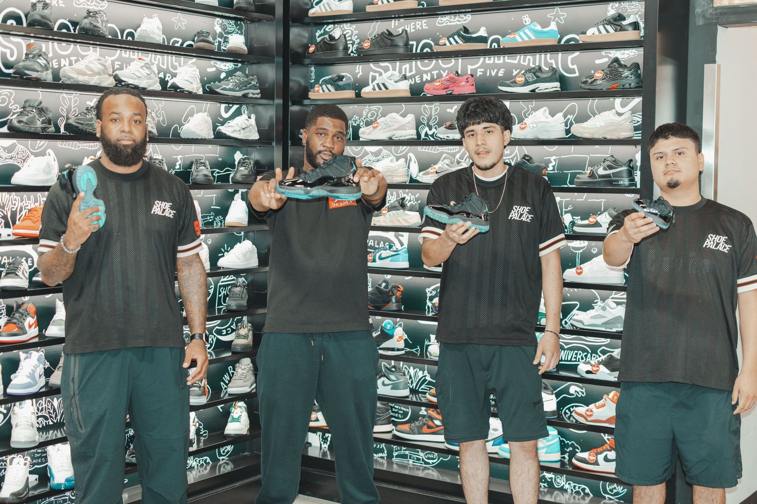Sneaker enthusiasts posing with their purchases in front of a wall of shoes.