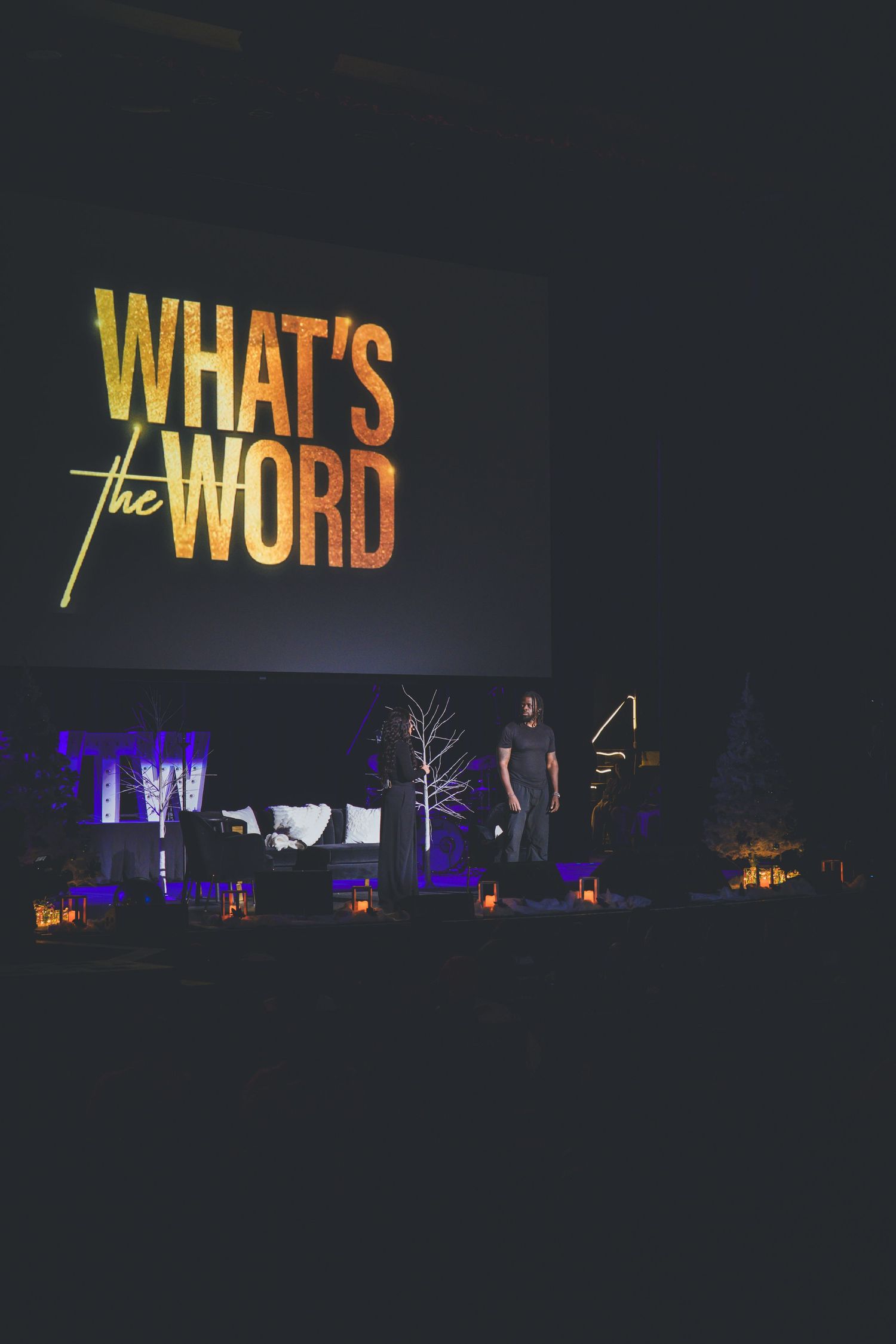 Yellow text display reading 'WHAT'S THE WORD' illuminated on dark stage with purple lighting.
