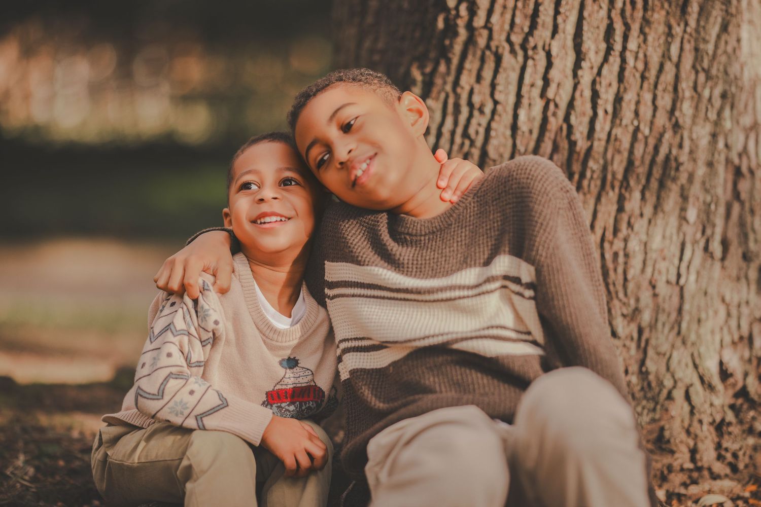 A parent and child share joyful moments together while sitting near a large tree trunk.