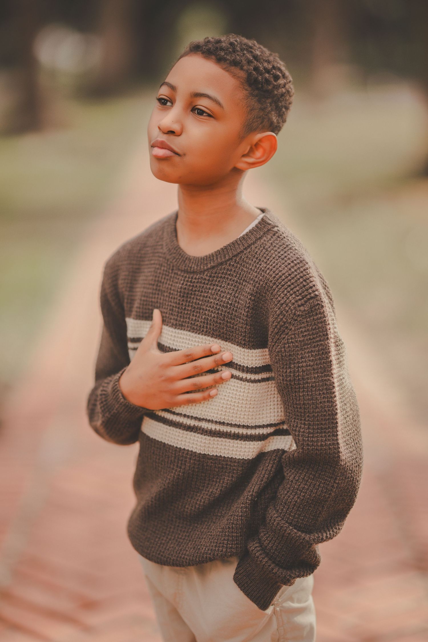 Child wearing a brown knit sweater with stripes poses expressively against a warm background.