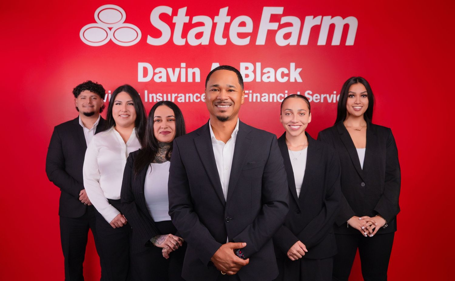 Insurance agency team members standing in front of red State Farm logo wall.
