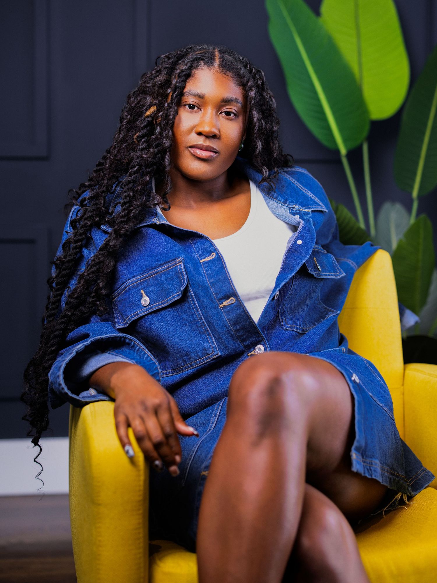 Fashion portrait series featuring a denim jacket and yellow chair against a dark background with tropical plants.