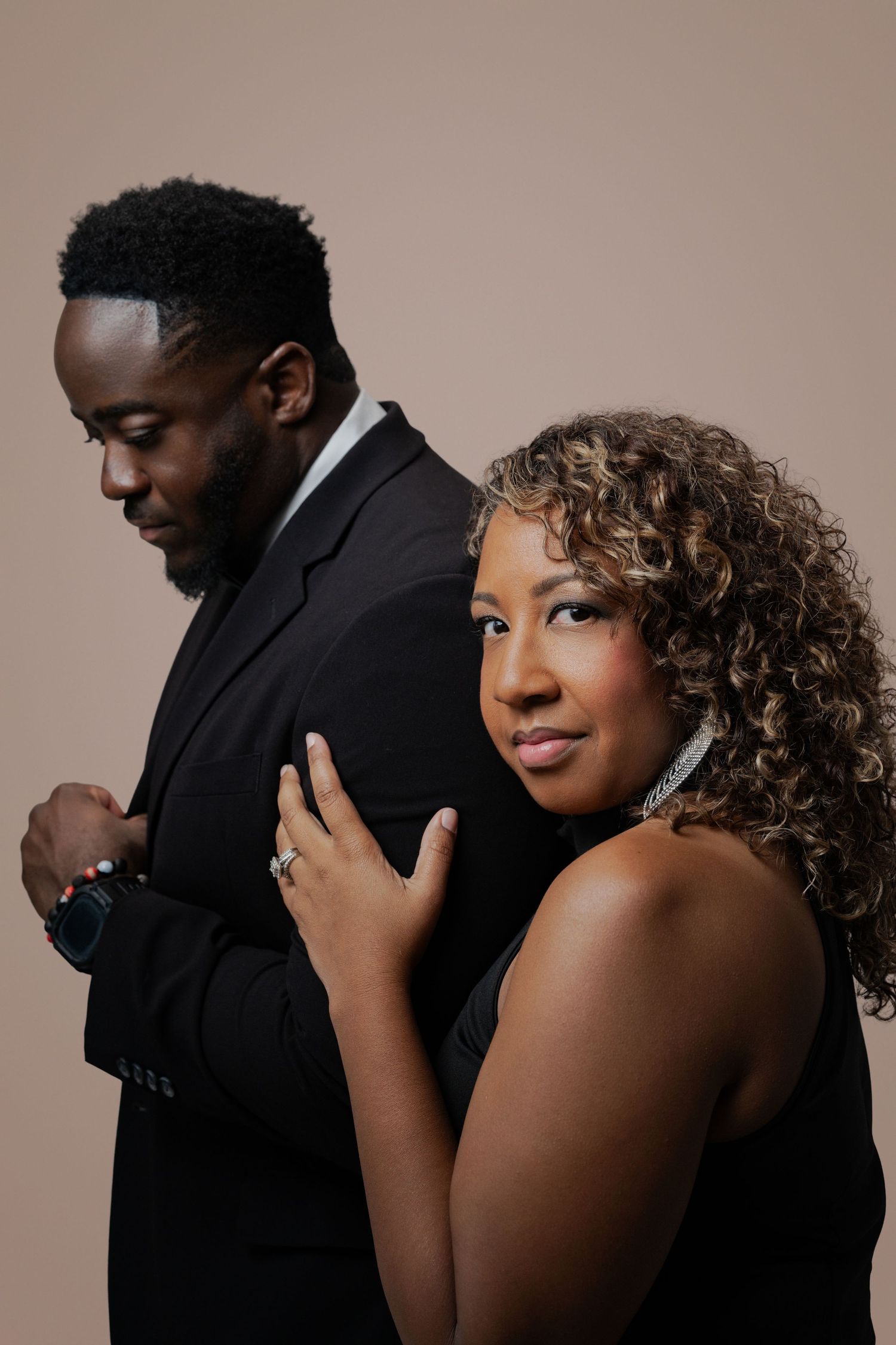 Couple embraces in intimate poses against neutral backdrop wearing formal black attire.