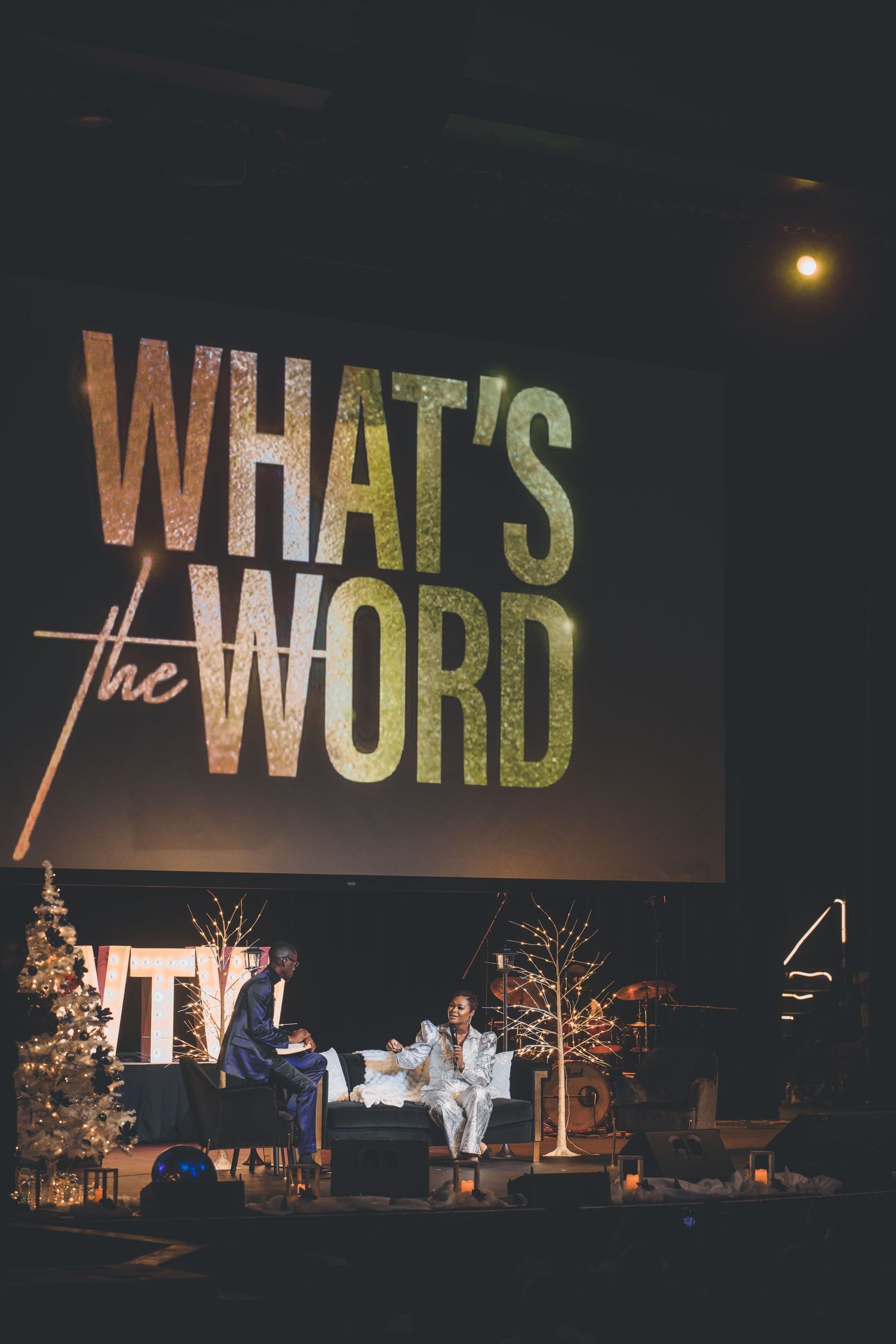 Stage setup with 'What's the Word' text display and Christmas decorations.