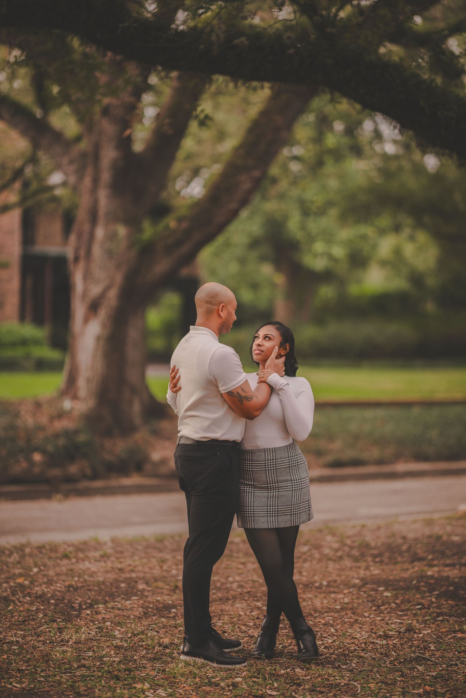 A couple embraces while walking together on a leaf-covered path in a scenic park setting.