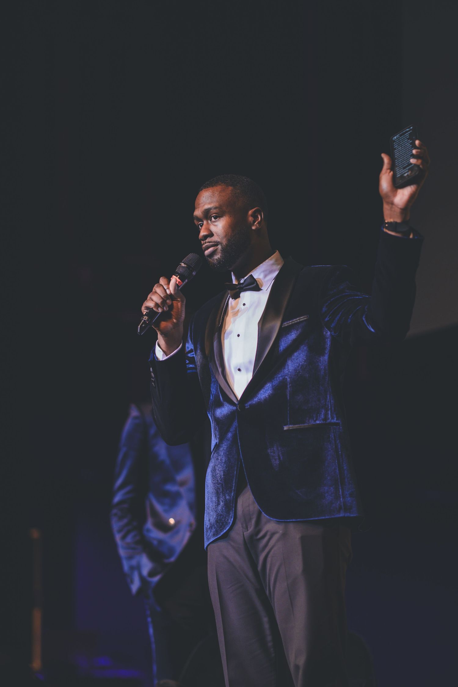Performer in blue suit jacket on darkly lit stage during an evening event.