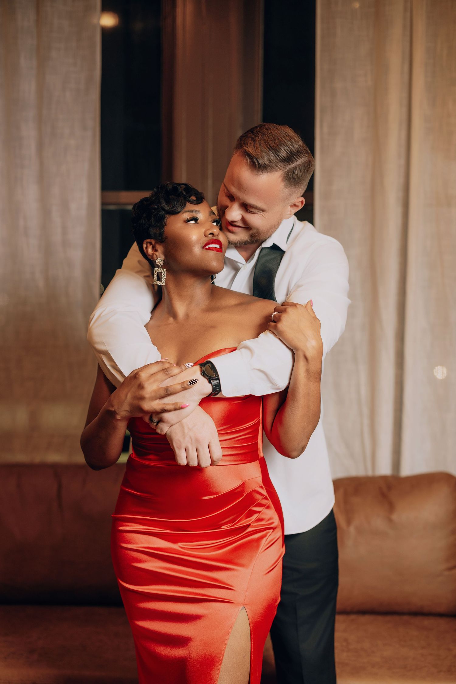 A couple in formal attire share an intimate dance moment, with the woman wearing a striking red satin dress.
