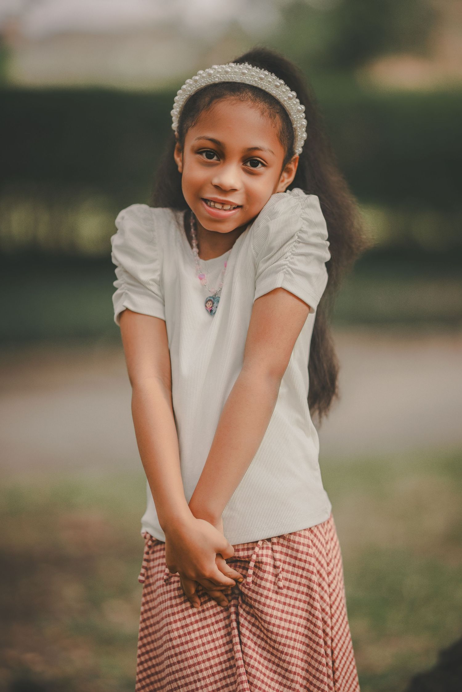 A child in a white top and checkered skirt plays joyfully outdoors.
