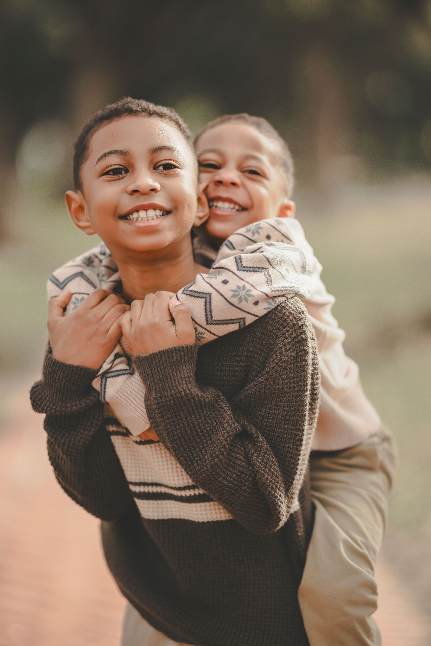 Two children in warm sweaters share a playful embrace outdoors on a sunny autumn day.