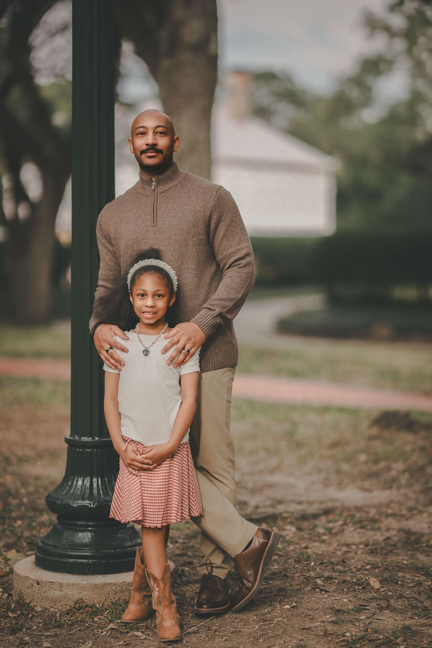 A parent and child pose together outdoors near a decorative lamp post in matching brown and neutral tones.