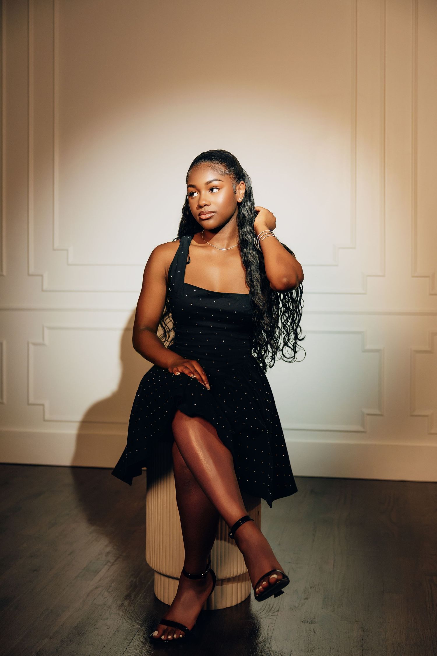 A series of artistic portrait photos showing a person in a black dress posing against a beige wall in dramatic lighting.