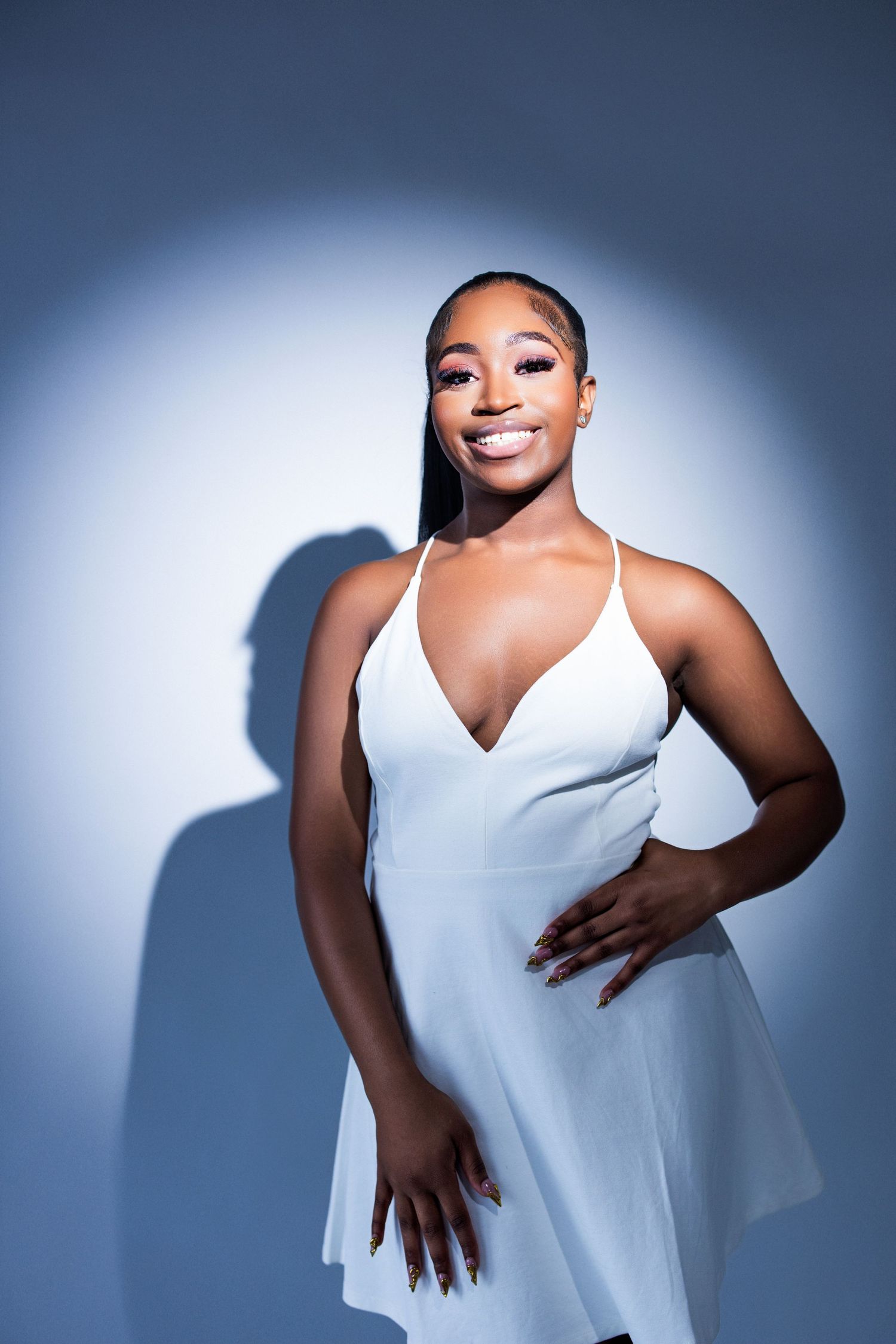 Woman in white top poses elegantly against blue backdrop with dramatic shadows.