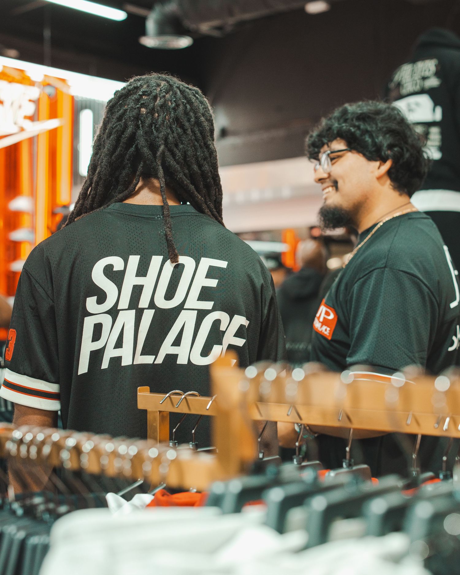 Staff members wearing black uniforms with text at sneaker store display counter.