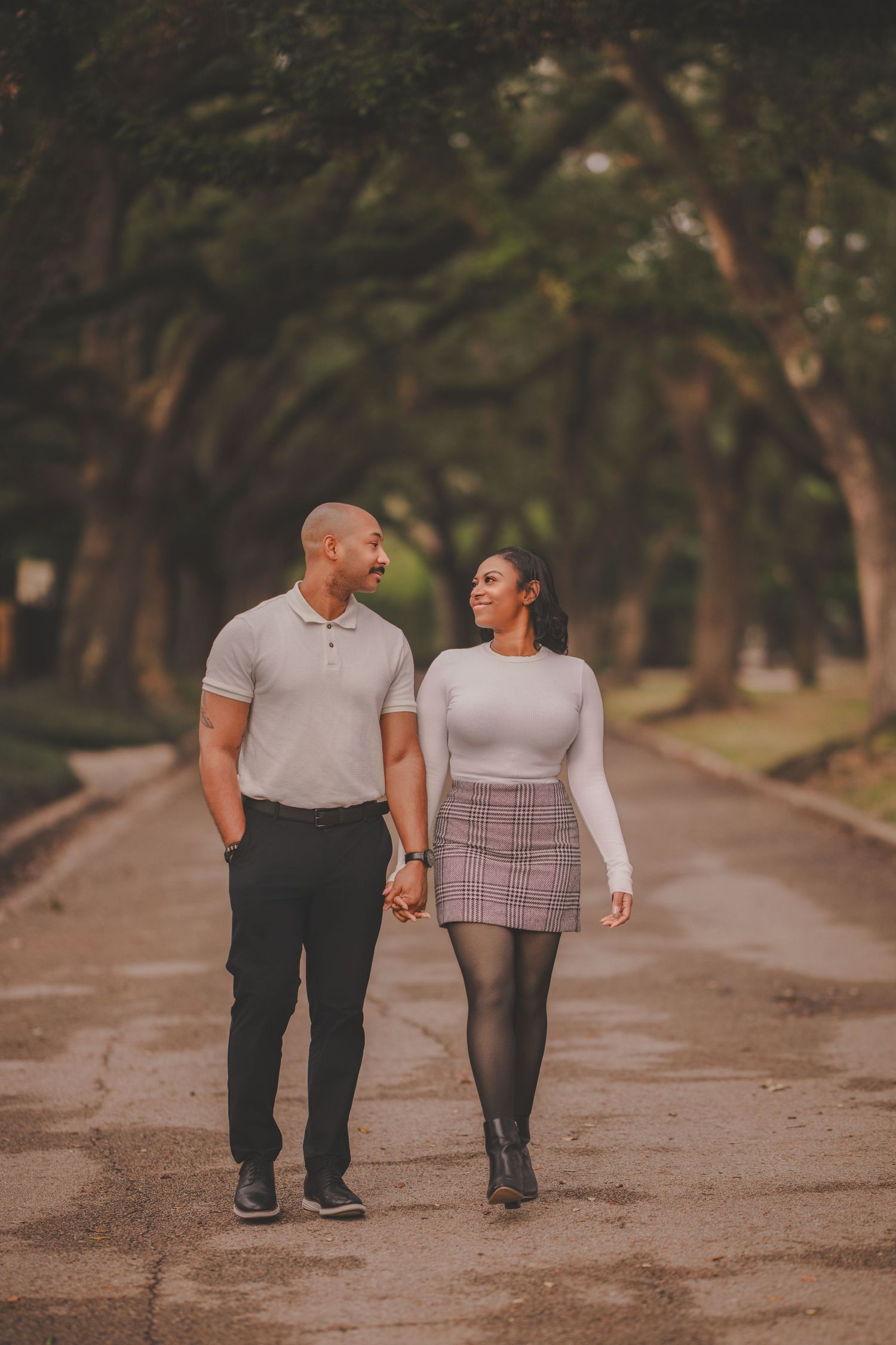 A couple takes a romantic stroll together on a tree-lined path during golden hour.