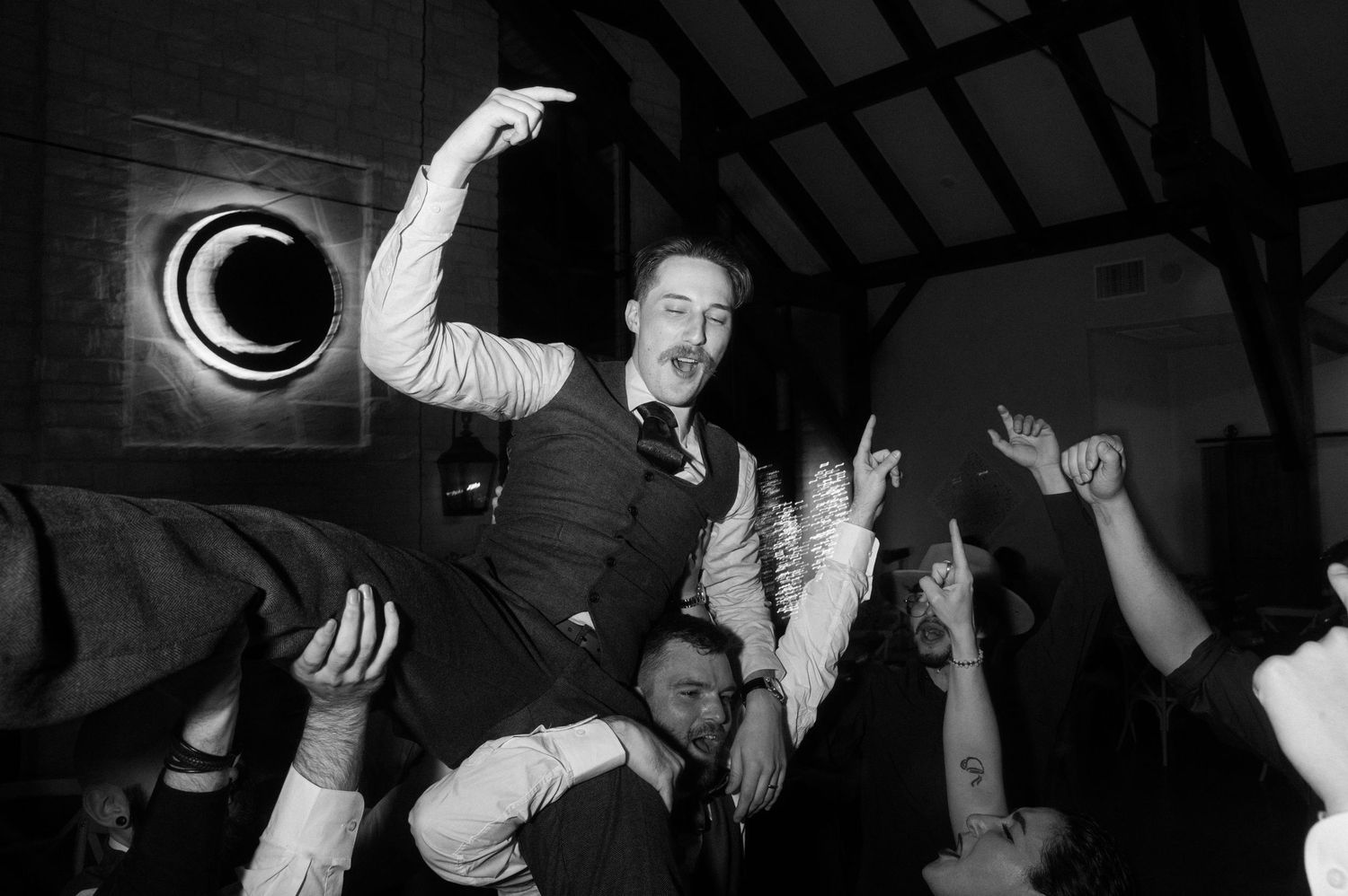 Black and white photo of groom celebrating on guests shoulders during a lively wedding reception dance party. Corpus Christi Wedding