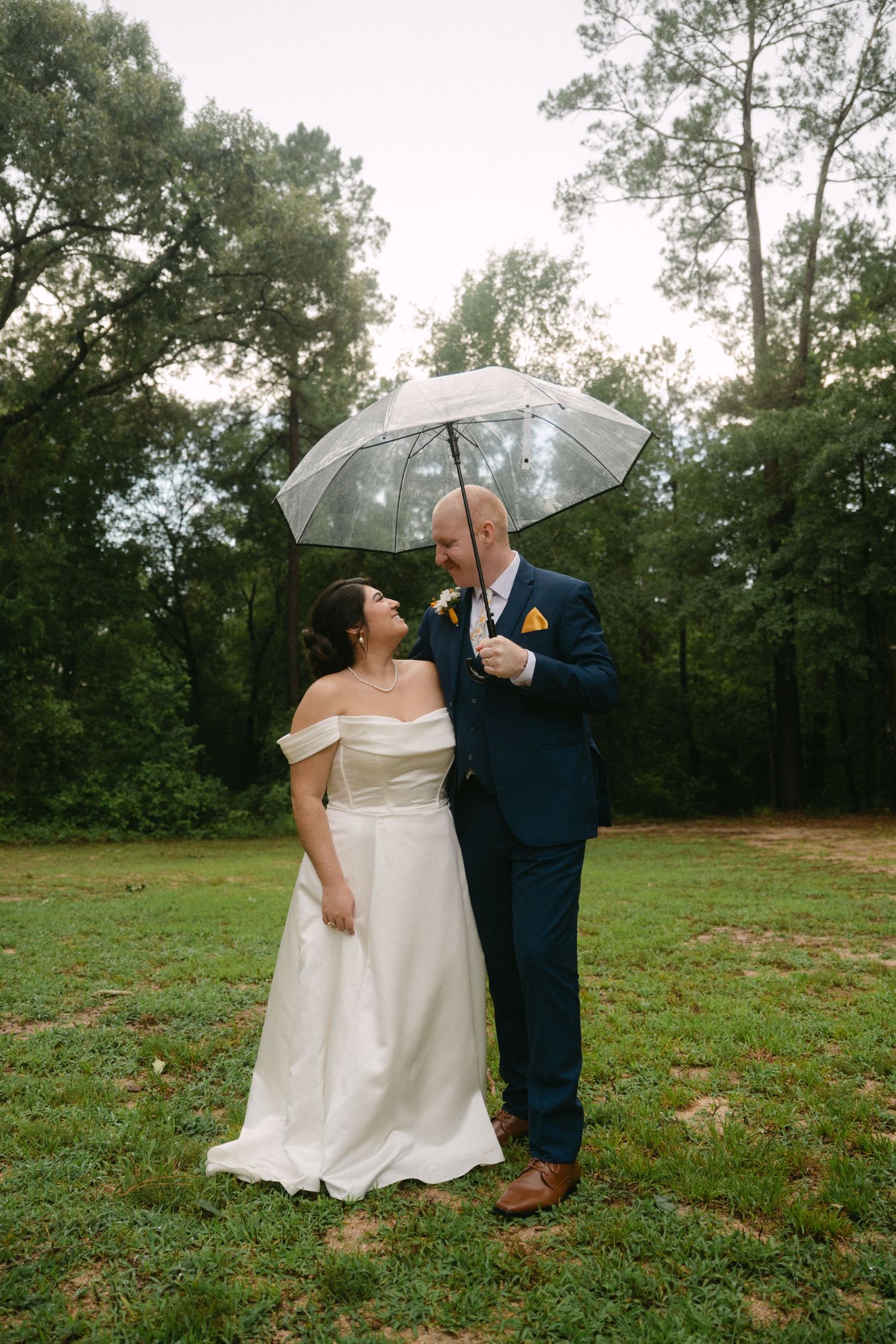 Bride and groom sharing a romantic moment under a clear umbrella on a lush green lawn. Corpus Christi Wedding Photographer