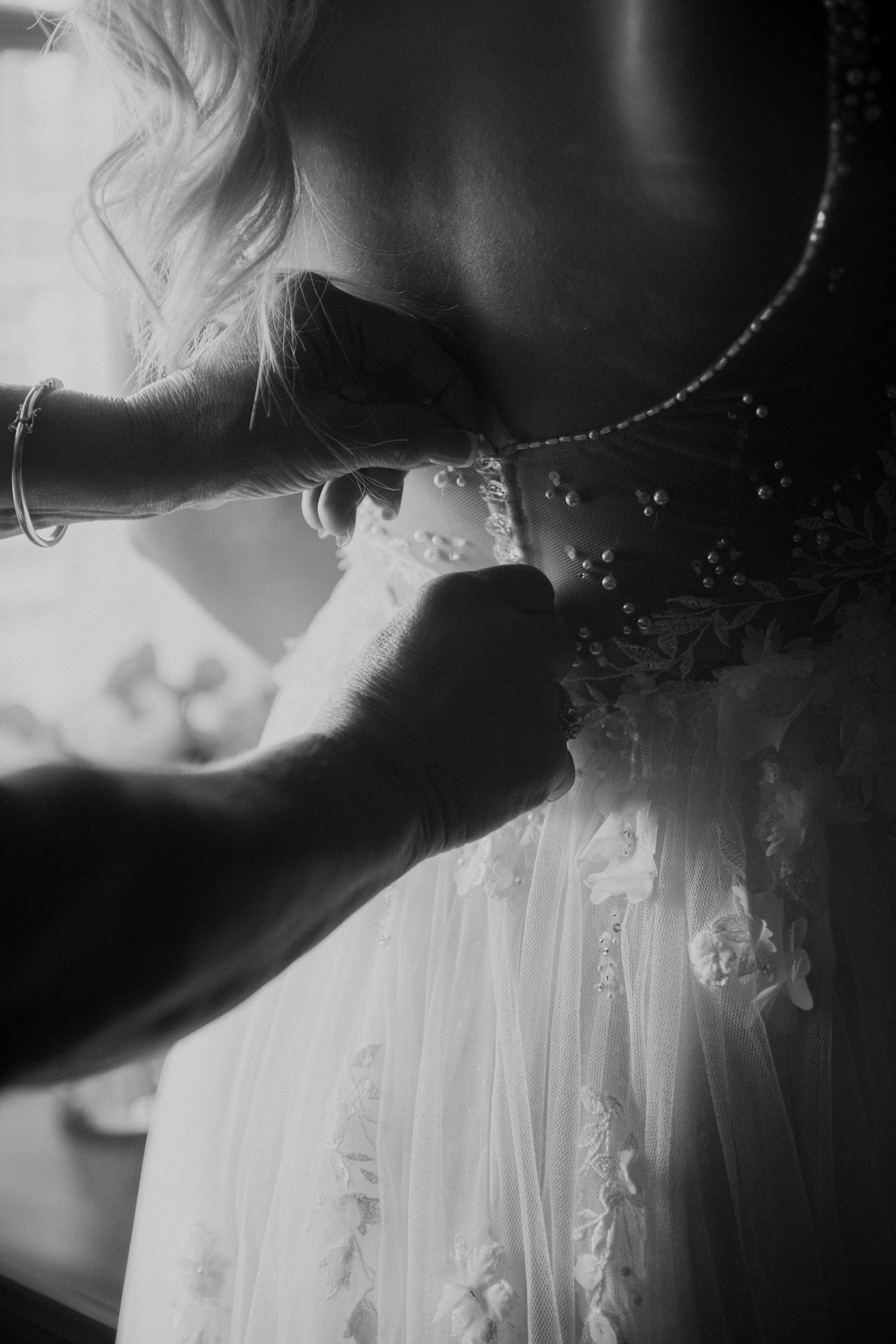 Black and white close-up of hands fastening pearl buttons on back of lace bridal gown before wedding ceremony. Corpus Christi Wedding Photog