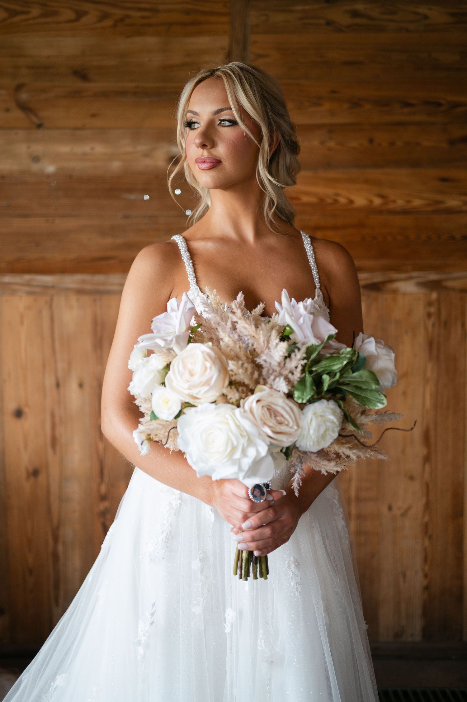 Bride in white lace gown holding bouquet of white roses and pampas grass in rustic barn setting. Corpus Christi Wedding Photographer